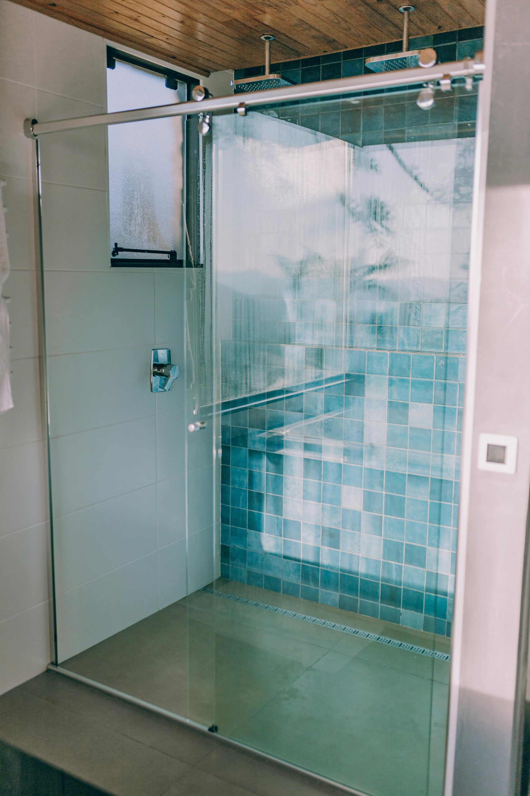 Elegant glass shower enclosure with modern blue tiles and natural light.