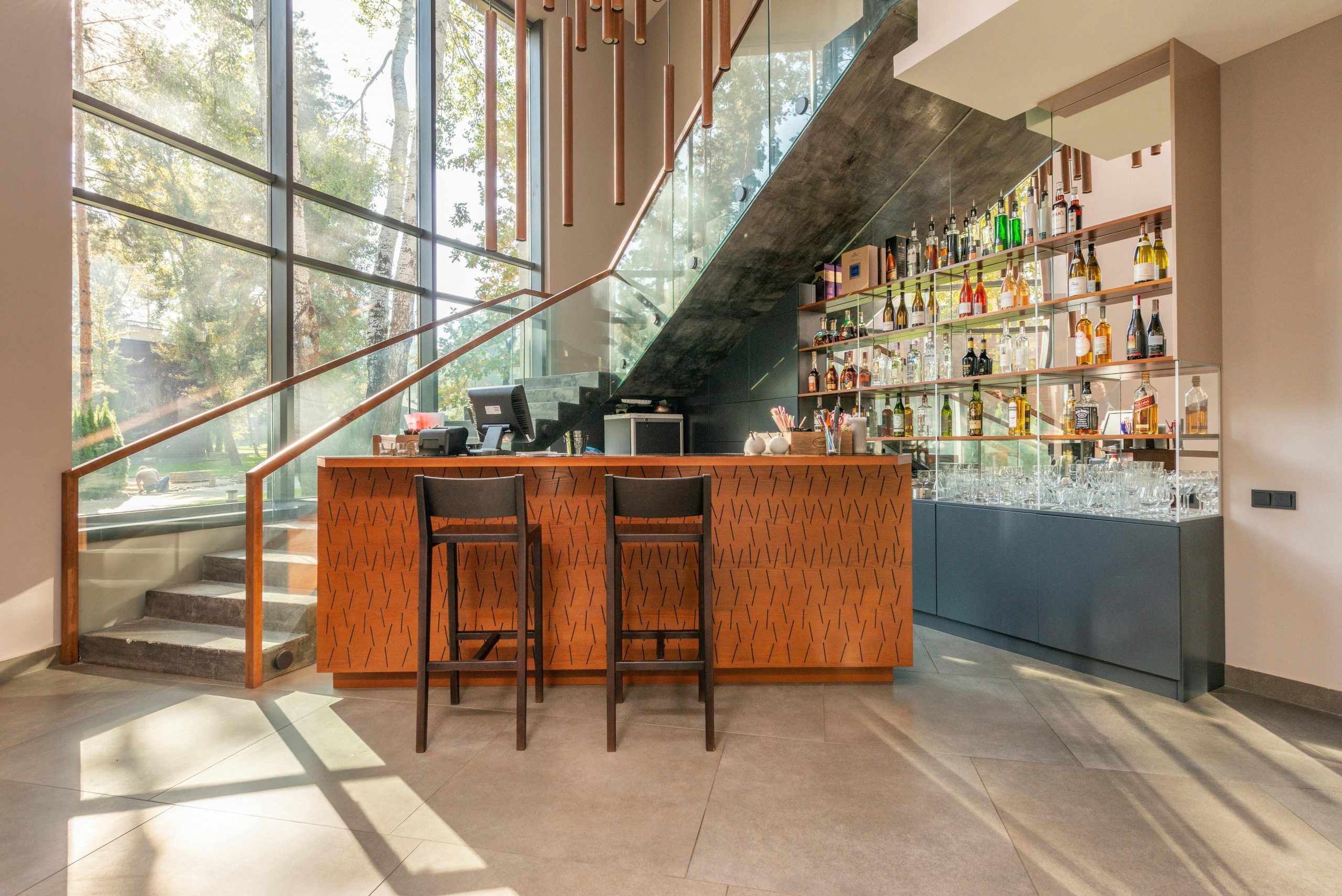 Elegant modern bar with glass walls, liquor shelves, and stylish seating in natural light.