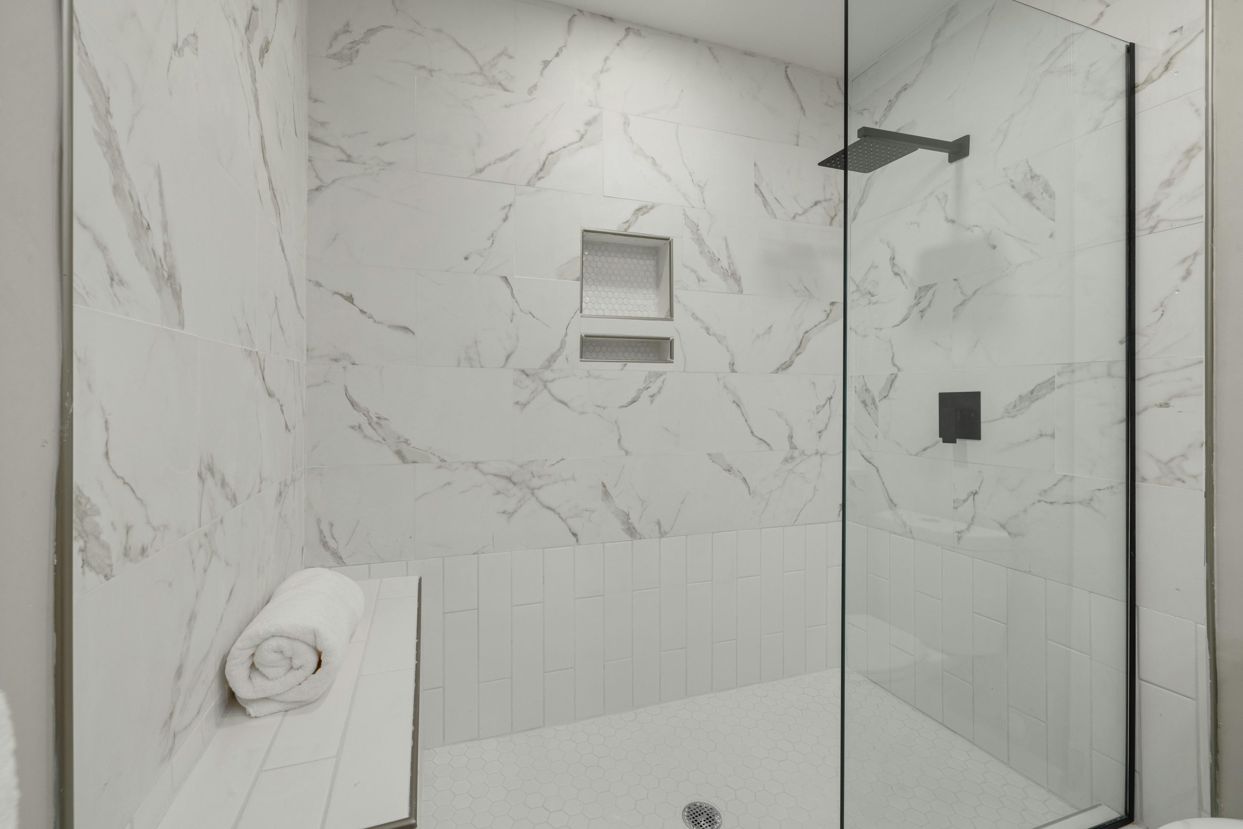 Elegant white marble shower with glass door, bench, and towel in modern bathroom.