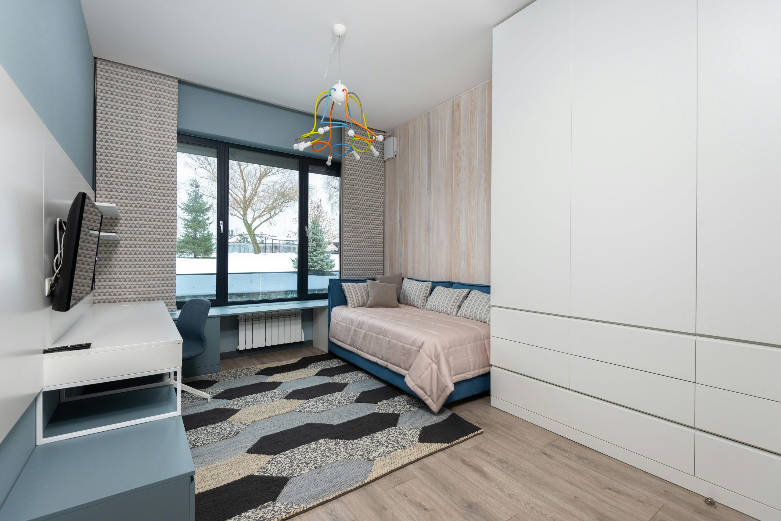 Interior of cozy bedroom with sofa bed and big wardrobe placed in front of table and TV hanging on wall