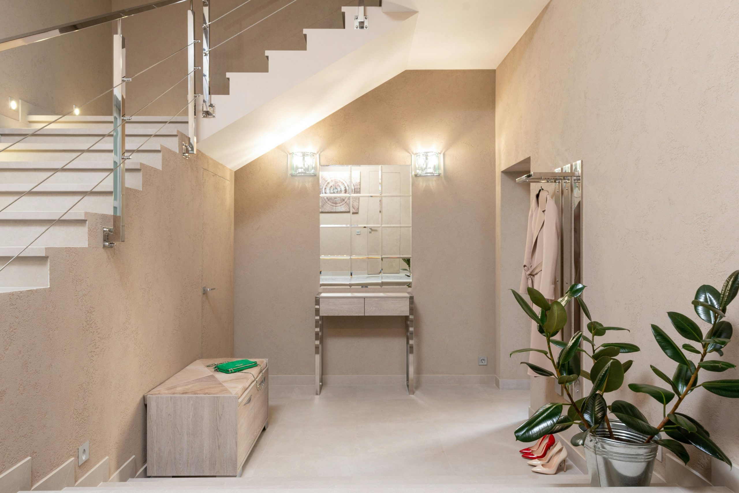 Interior of light contemporary apartment hallway with beige walls and staircase to second floor and glowing lamps on sides of mirror
