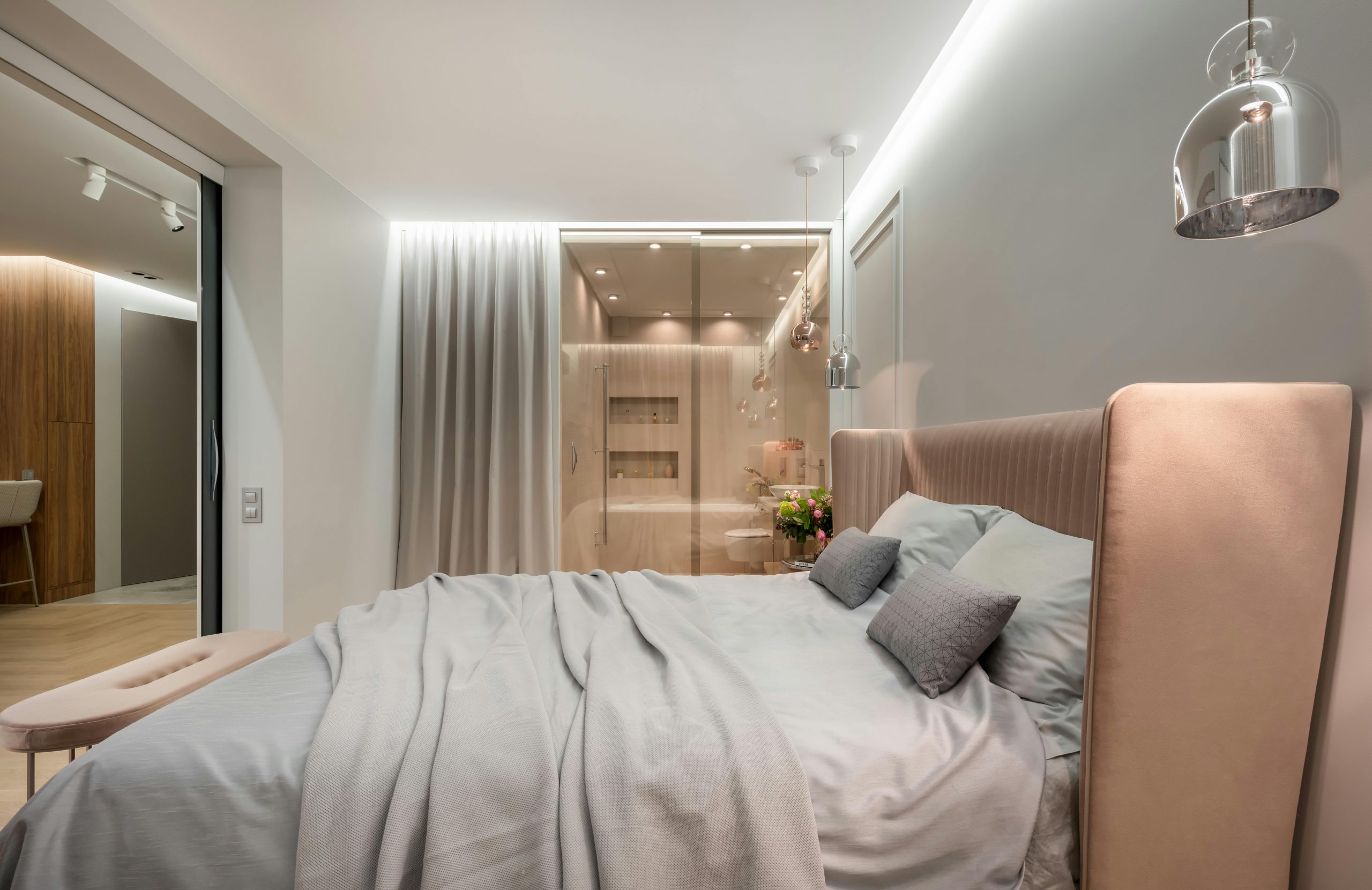Interior of modern light bedroom with pillows and blanket on bed under lamps next to pouf near glass wall with curtain