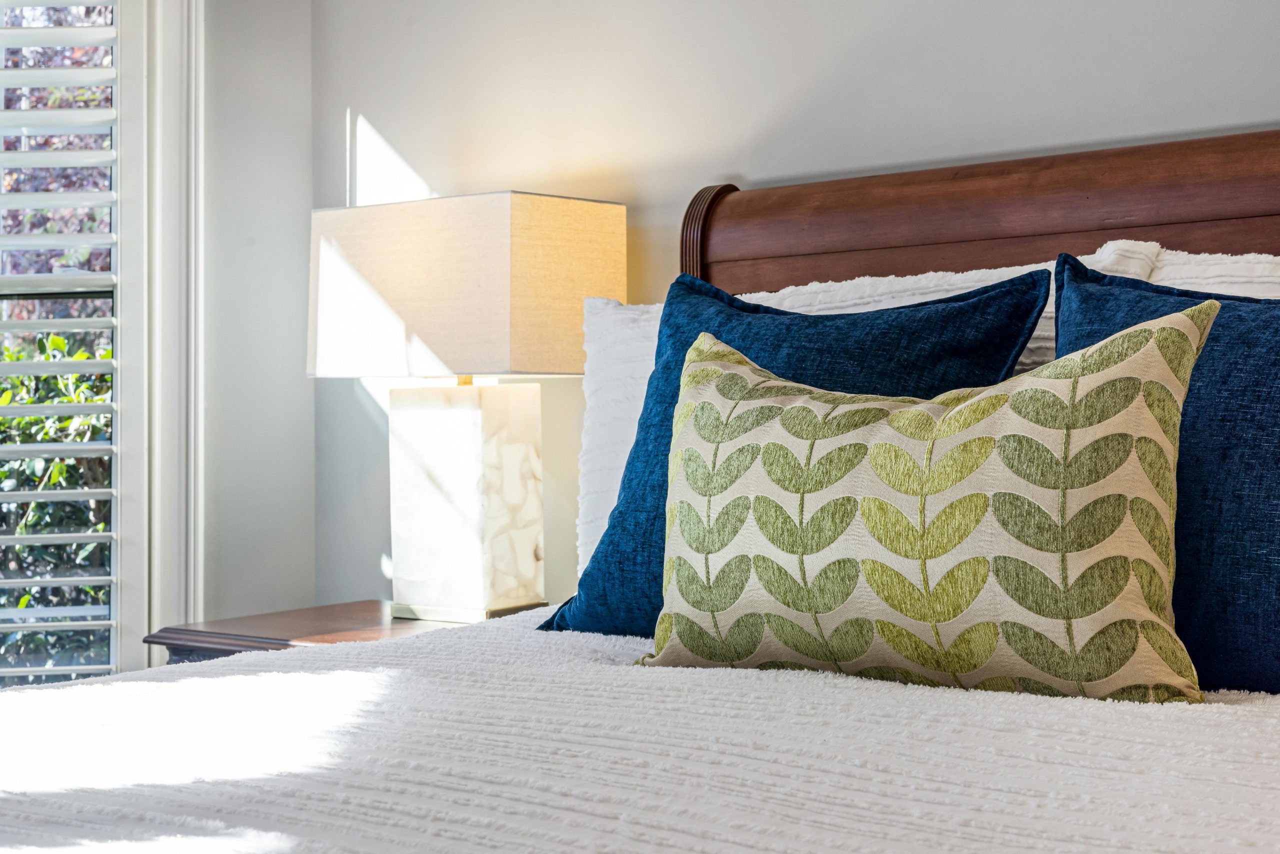 Inviting bedroom with decorative pillows and warm sunlight filtering through windows.