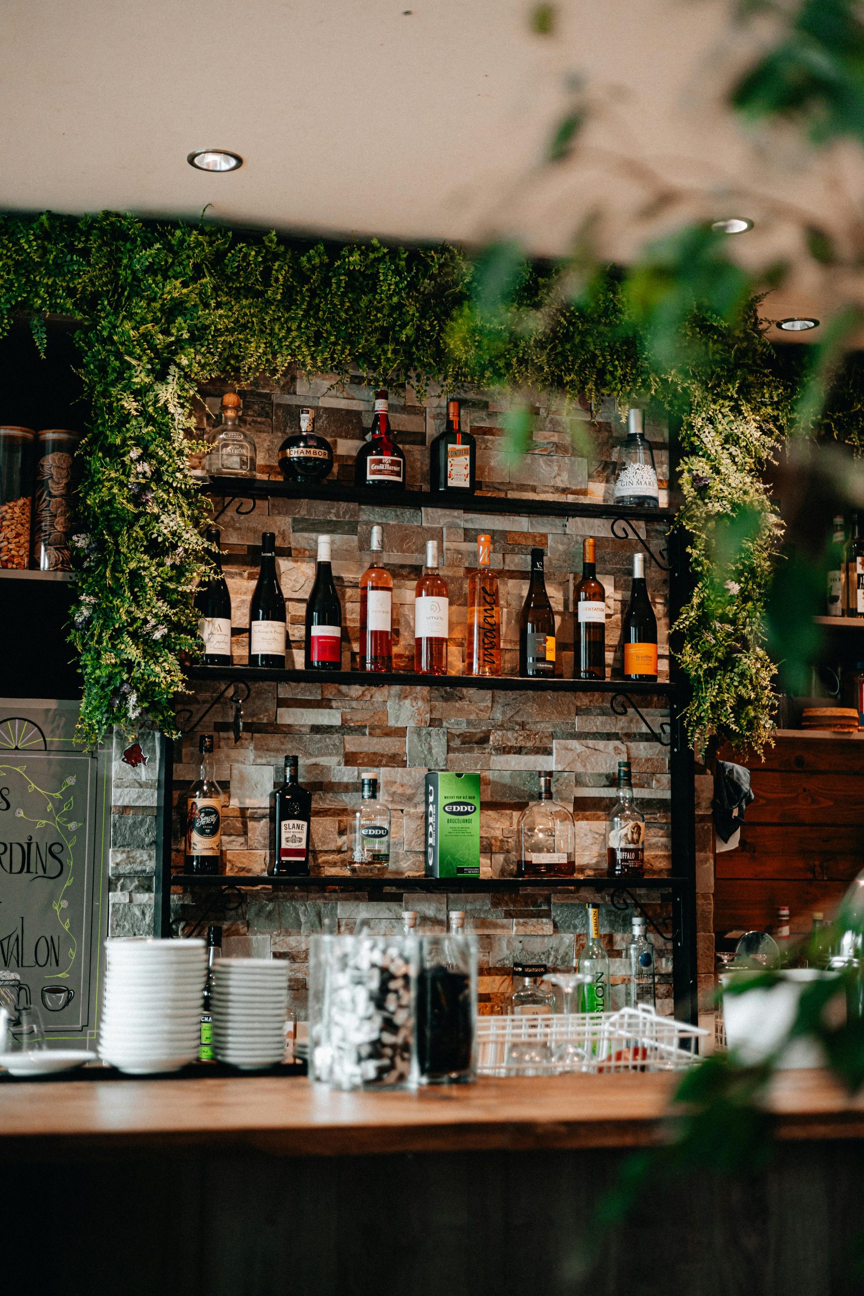 Inviting rustic bar with lush greenery and diverse alcohol selection, perfect for social gatherings.