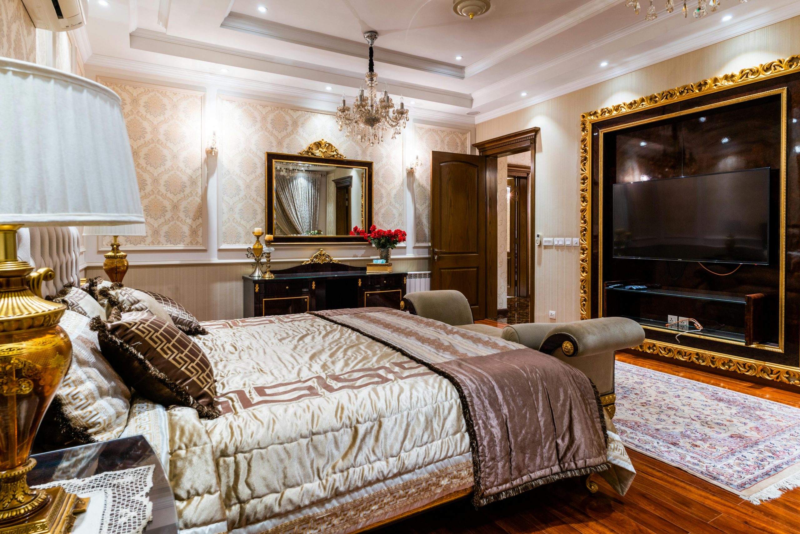 Luxurious hotel bedroom featuring elegant decor, large mirror, chandelier, and gold accents.
