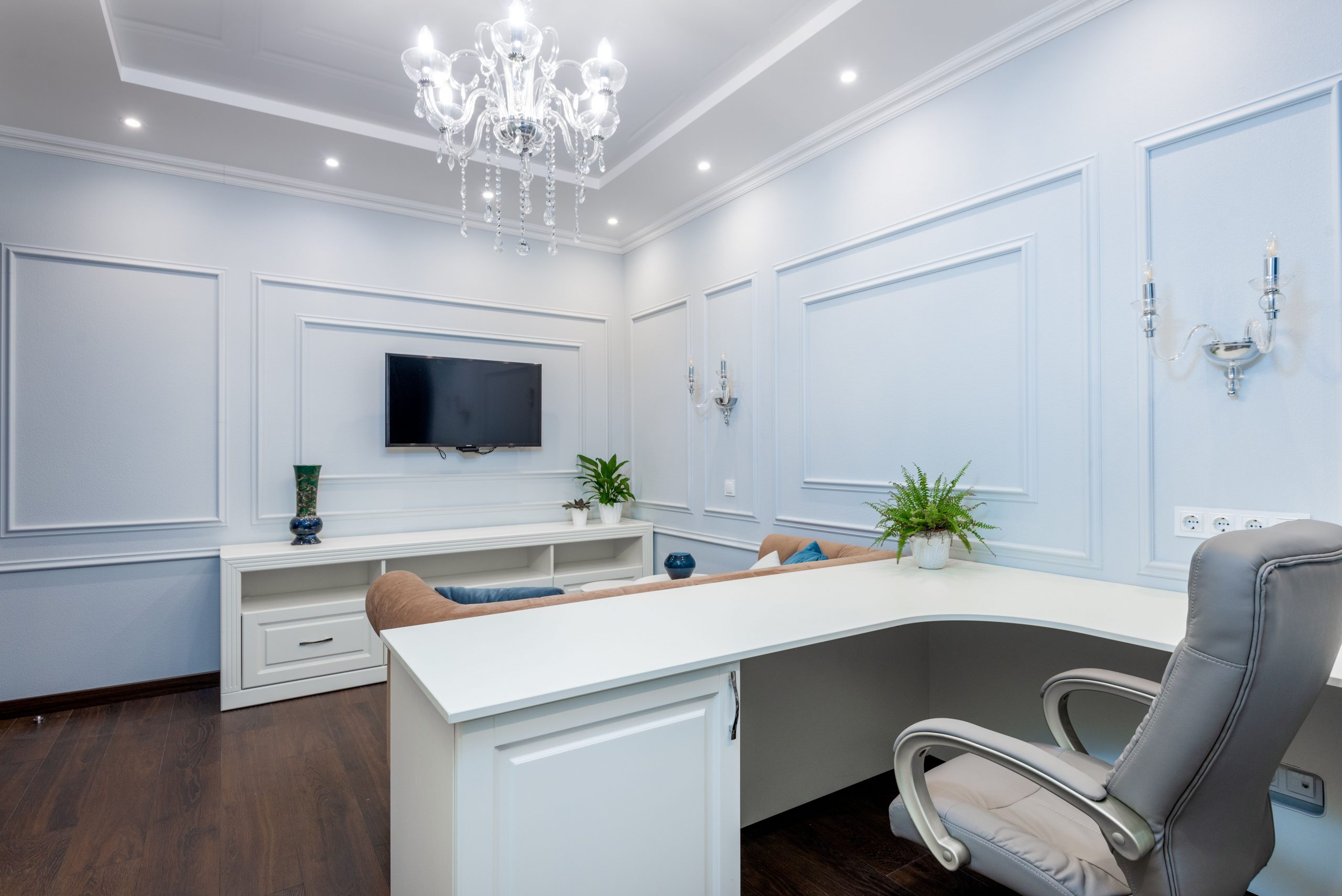 Luxurious office interior with minimalist design, featuring white furniture, chandelier, and flat-screen TV.