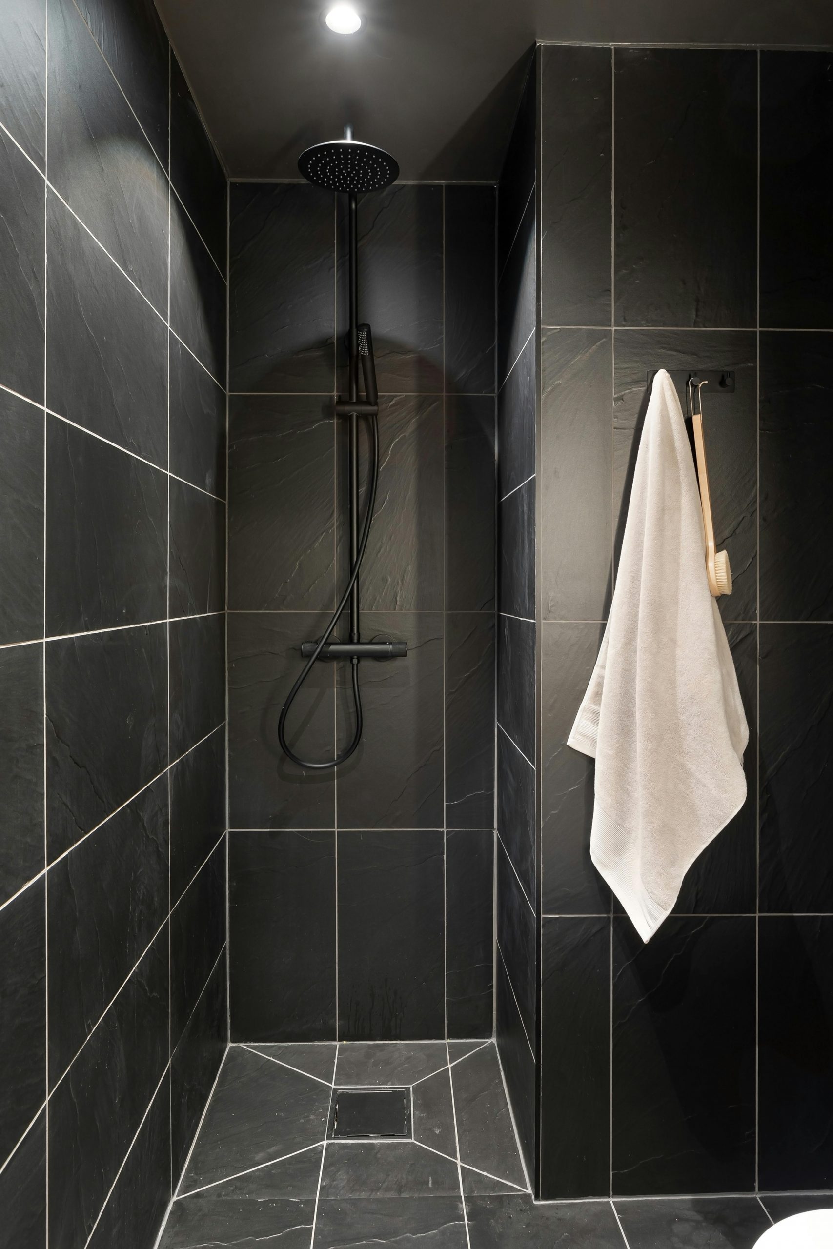 Minimalist black tiled shower with hanging white towel and modern fixtures.