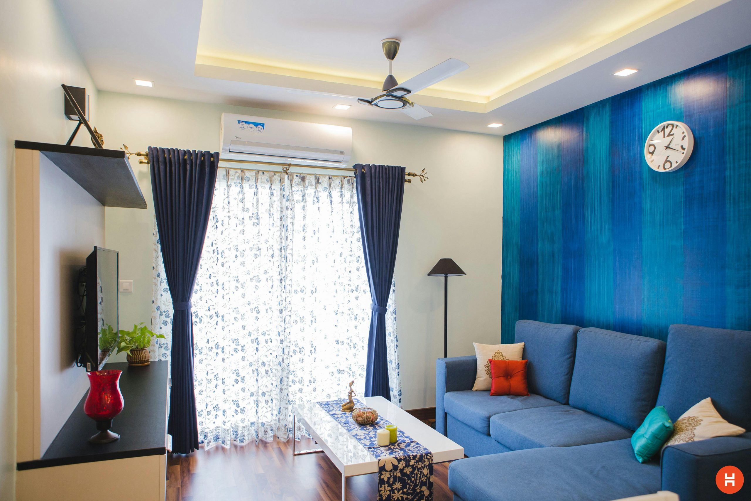 Modern living room with blue accents, featuring a sofa, wall clock, and natural light.