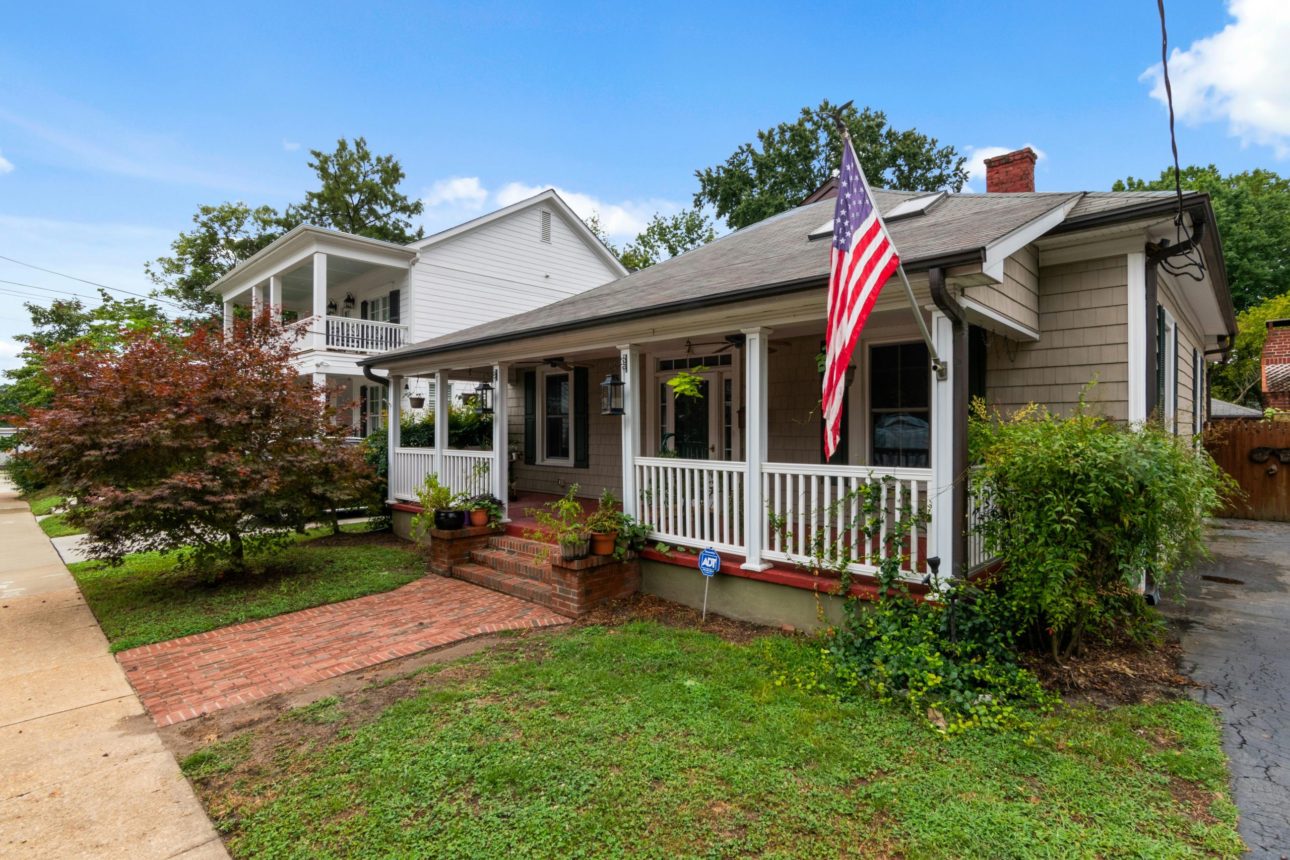 Quaint American bungalow with flag and lush garden under a blue sky.