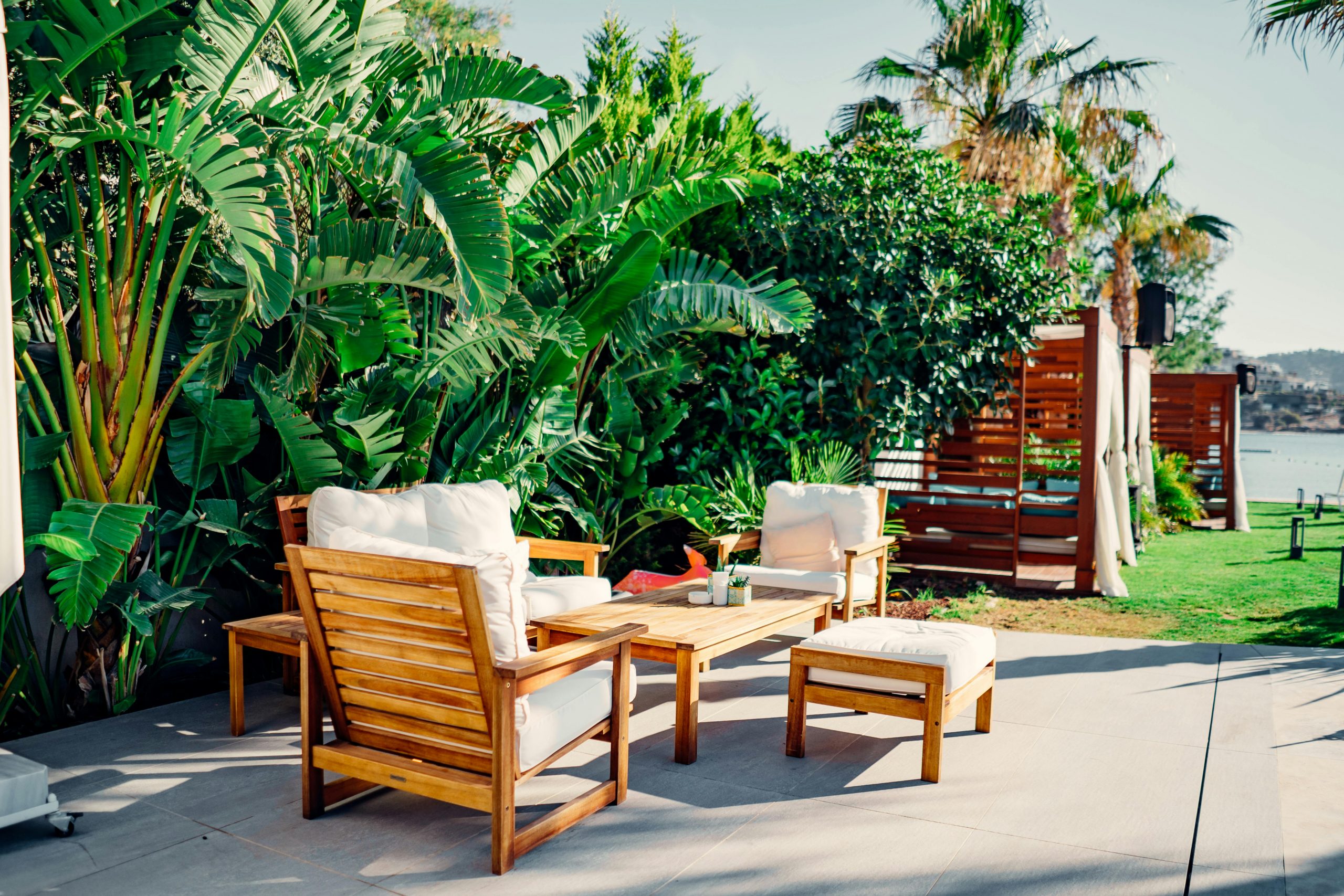 Relaxing outdoor patio with wooden furniture surrounded by lush greenery and tropical plants.