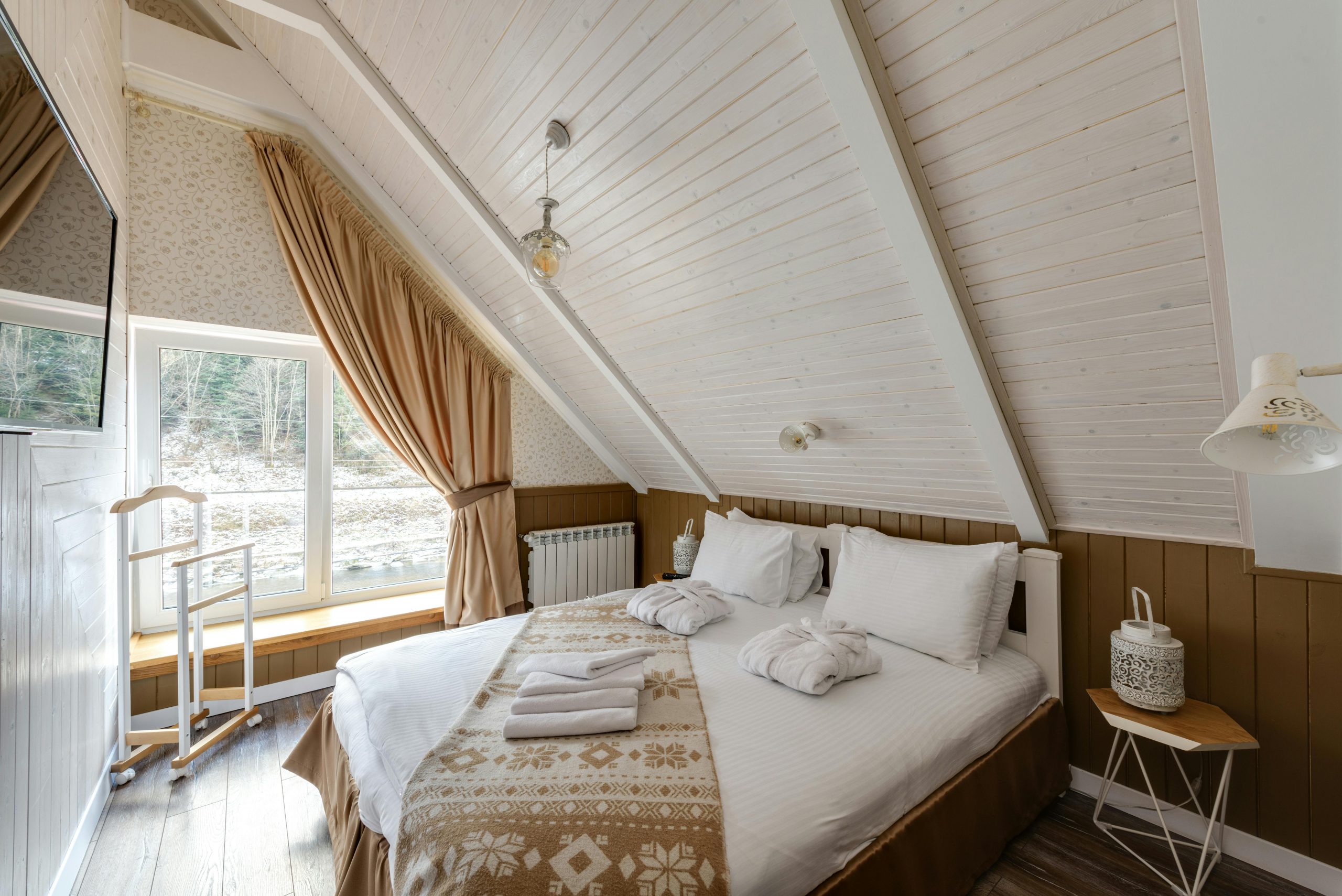 Rustic attic bedroom featuring a double bed, elegant decor, and a scenic view through a large window.