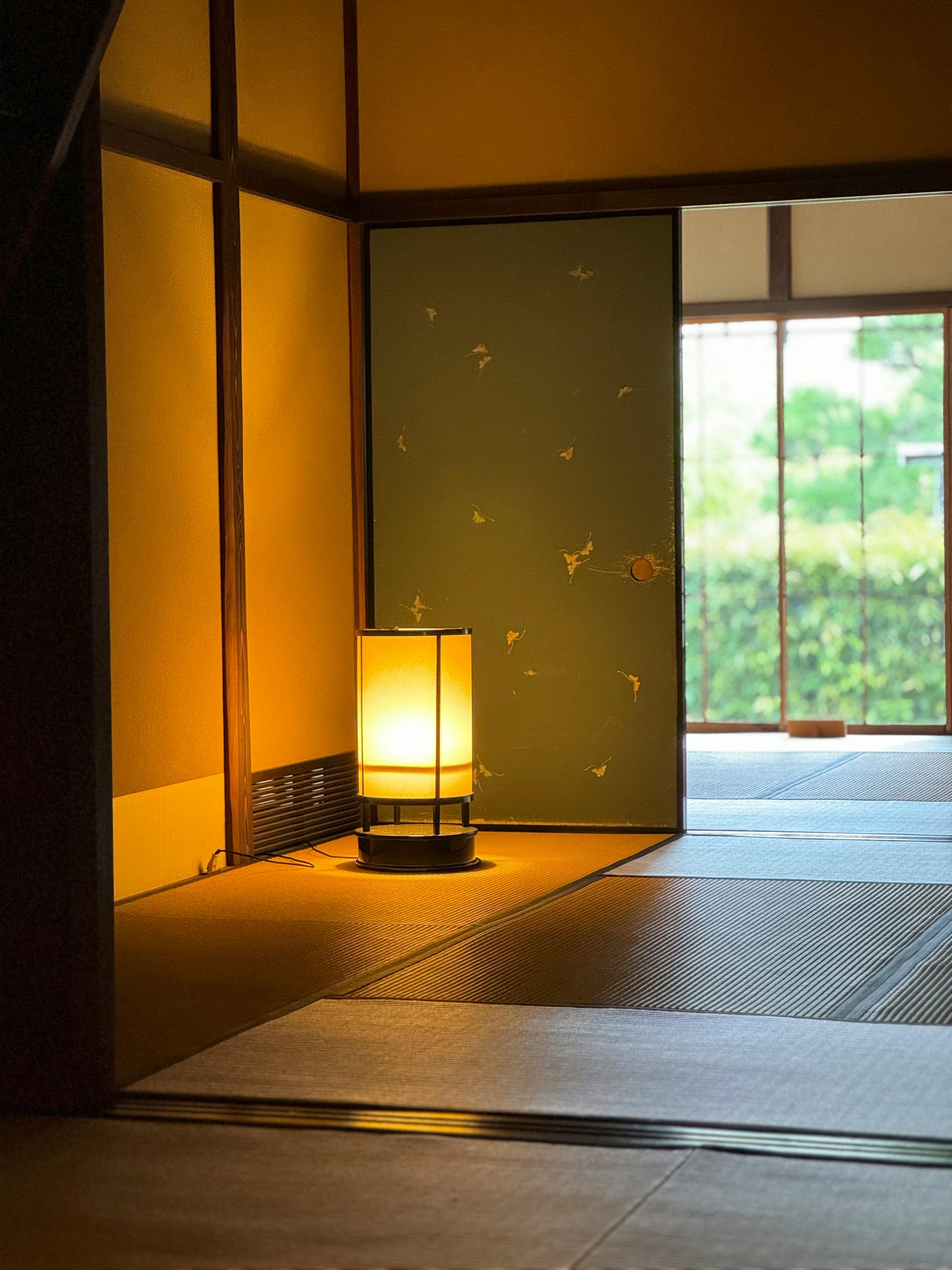 Serene Japanese room featuring tatami mats and a glowing lamp with an open view to the garden.