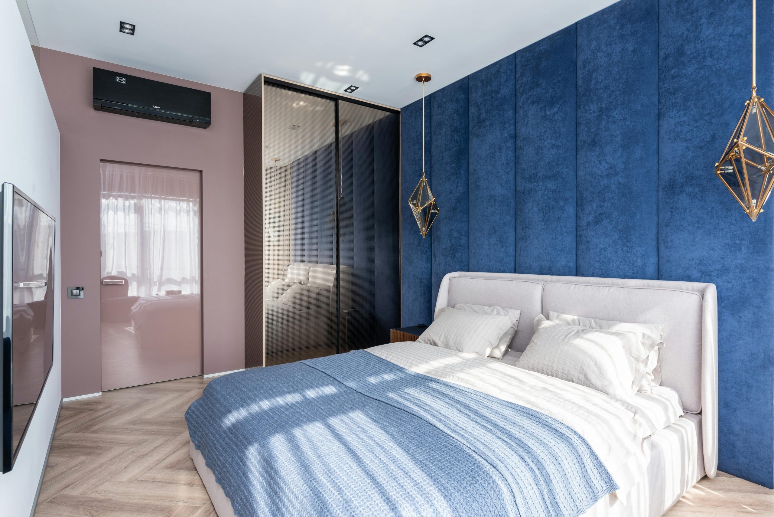 Soft bed with blanket placed against white wall with TV in modern bedroom with wardrobe and door near blue wall