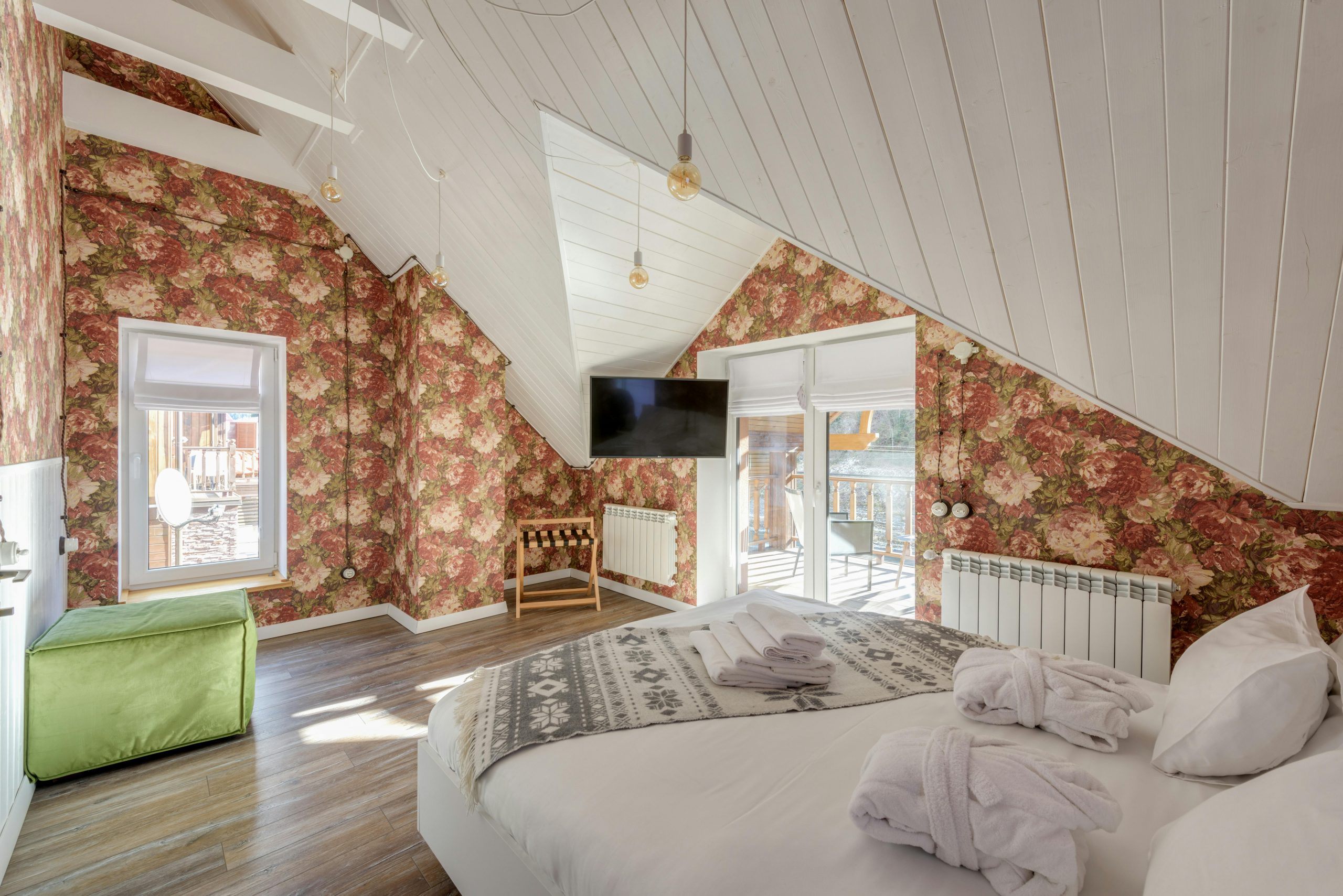 Spacious attic bedroom featuring floral wallpaper, cozy bed, and balcony view.