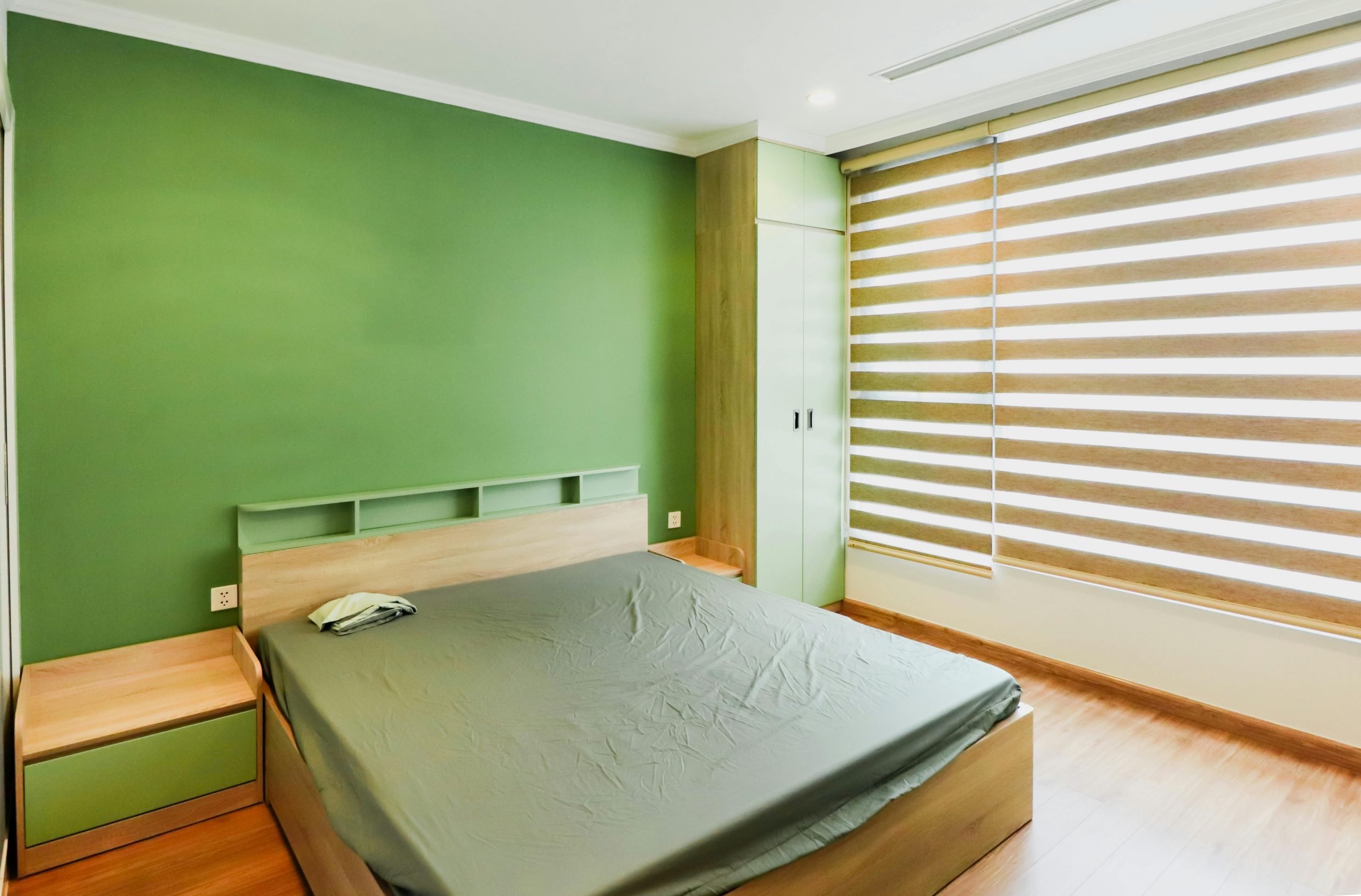 Spacious bedroom featuring a green accent wall, minimalistic furniture, and striped blinds.