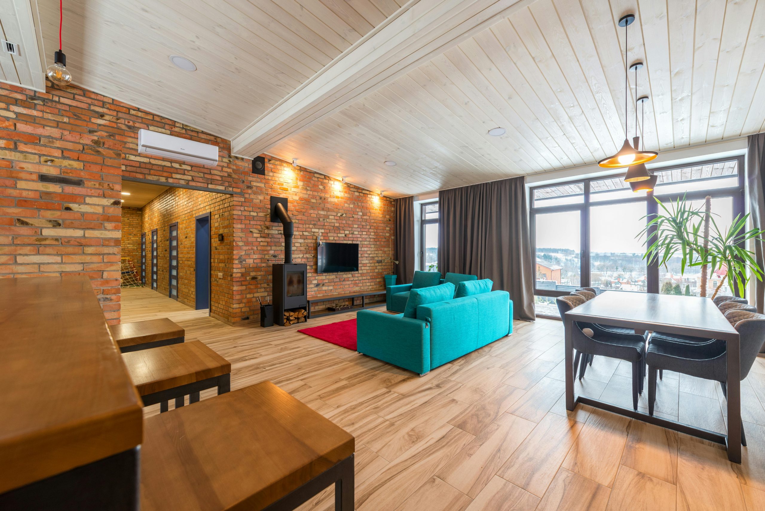 Spacious modern living room featuring a brick wall, teal sofa, and large windows.