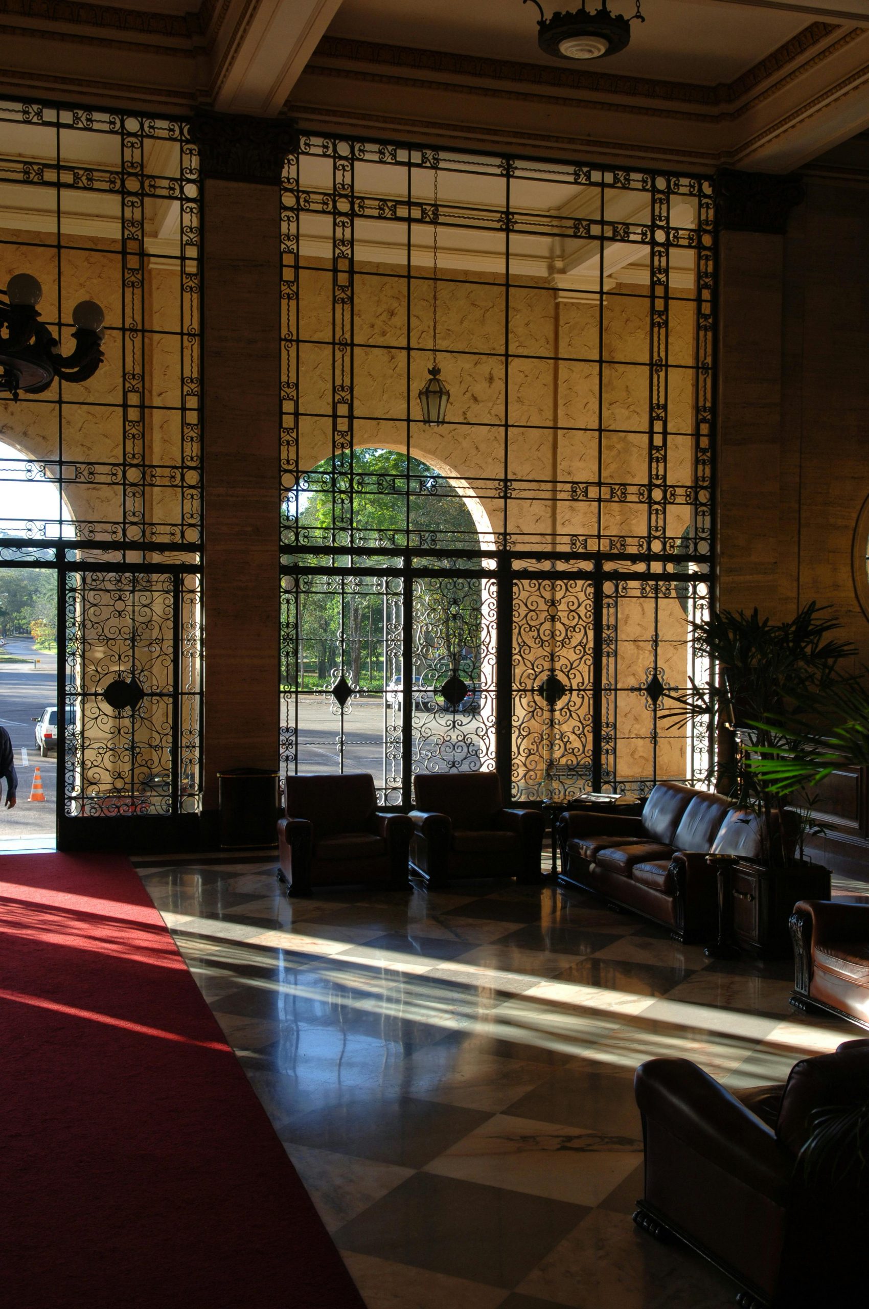 Sunlight streams through ornate windows, illuminating a grand hotel lobby with marble floors and leather seating.