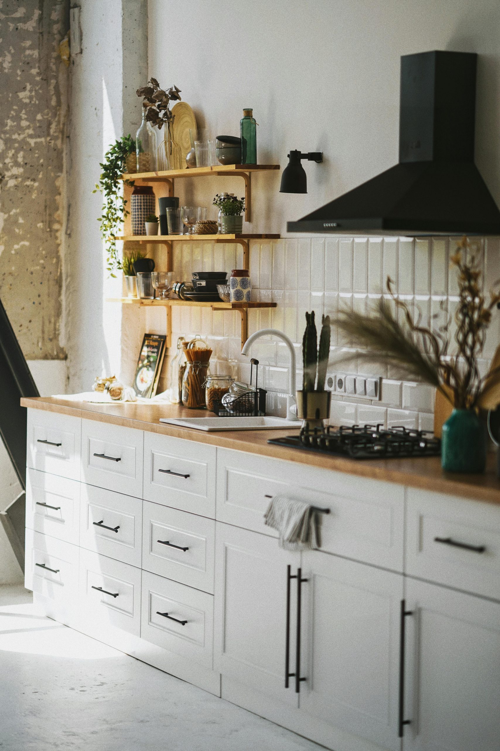 Sunlit modern kitchen in Scandinavian style with wooden shelves and white cabinetry.