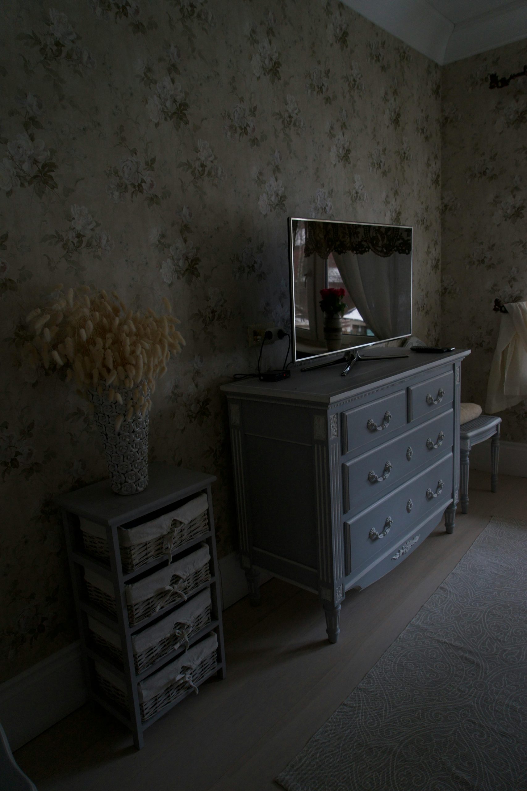 Vintage bedroom decor featuring antique dresser and floral wallpaper.
