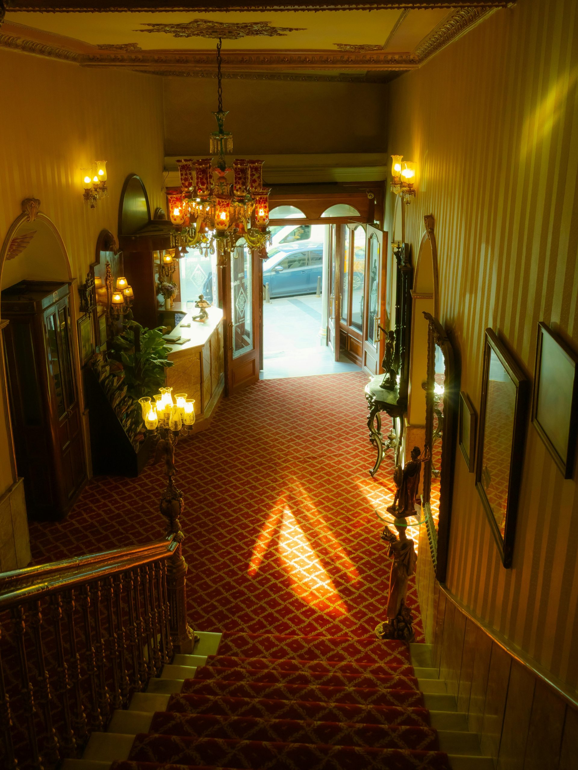 Warmly lit vintage hotel lobby in İstanbul with ornate decor and rich red carpet.