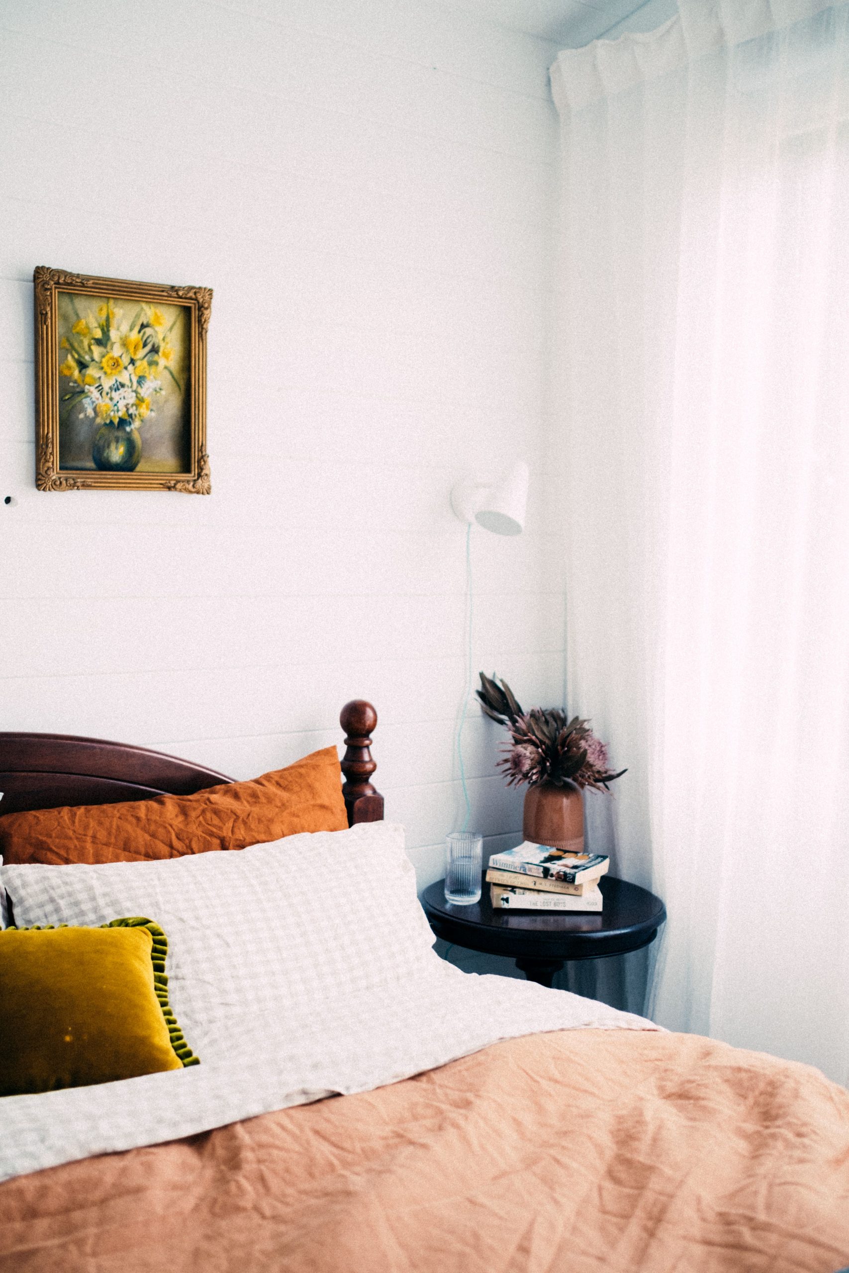 A beautifully decorated bedroom with a wooden bed, pillows, and a side table, bathed in soft natural light.