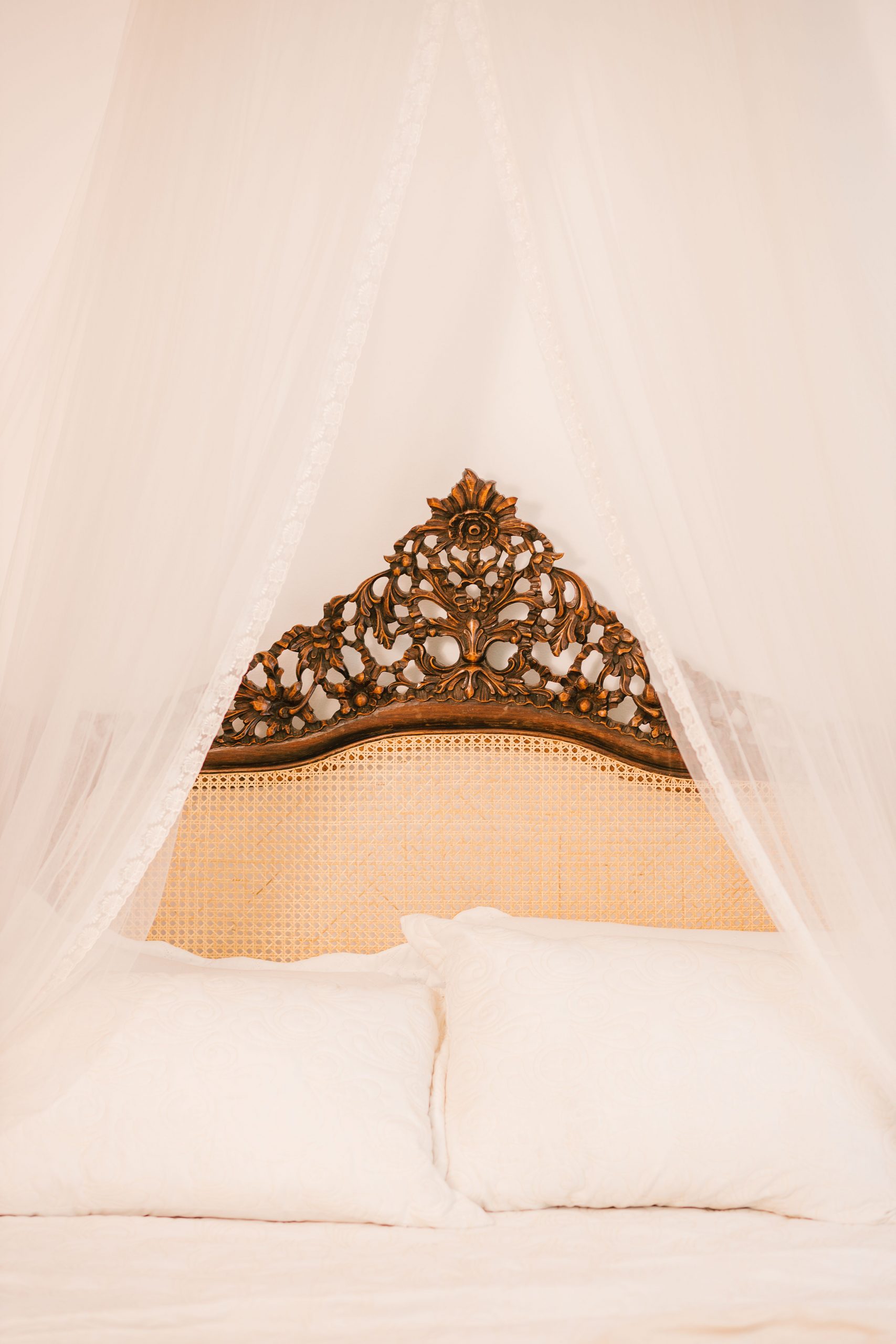 A beautifully elegant canopy bed featuring an intricately carved wooden headboard and soft white pillows.