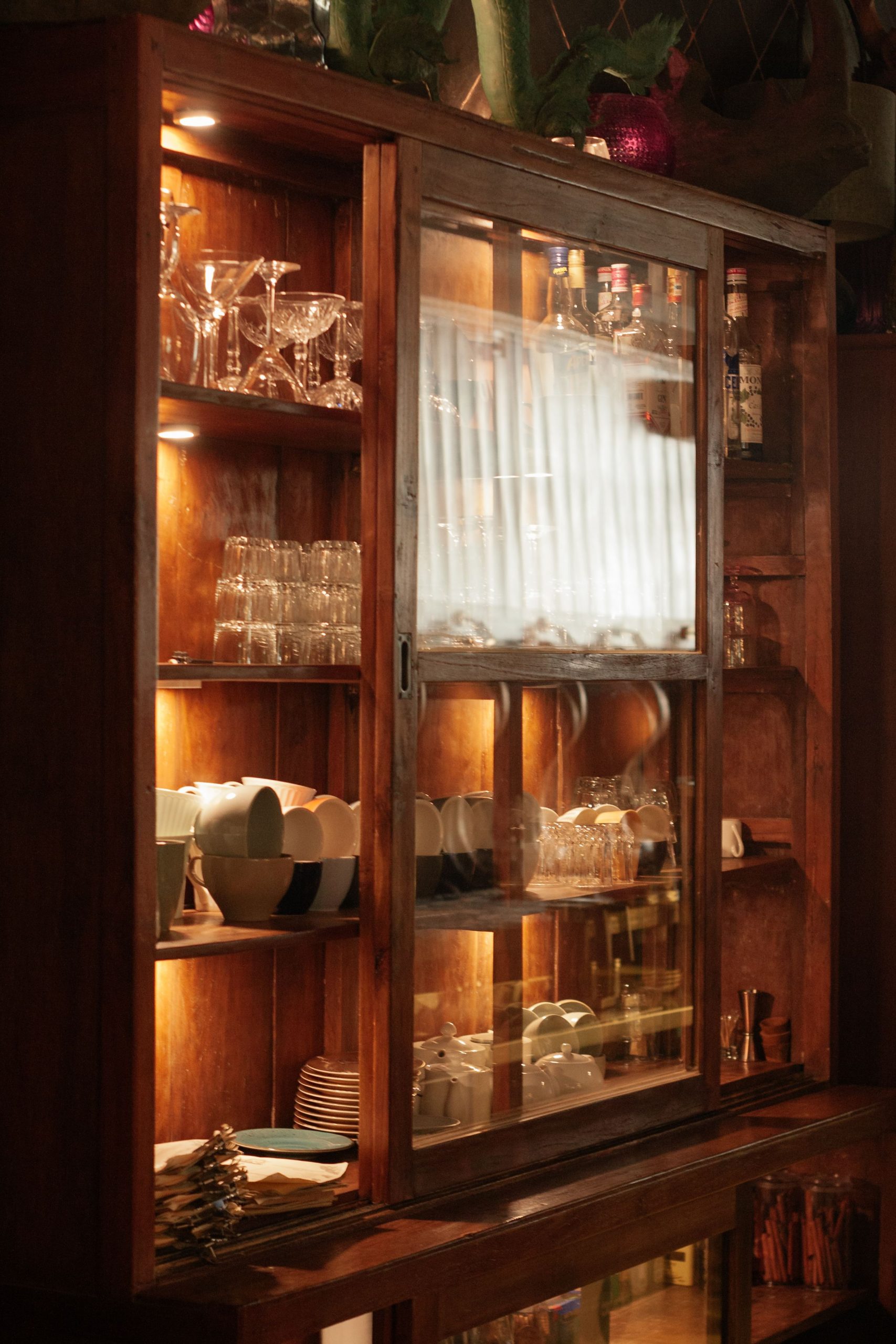 A beautifully lit wooden cabinet showcasing an elegant collection of glassware and porcelain.