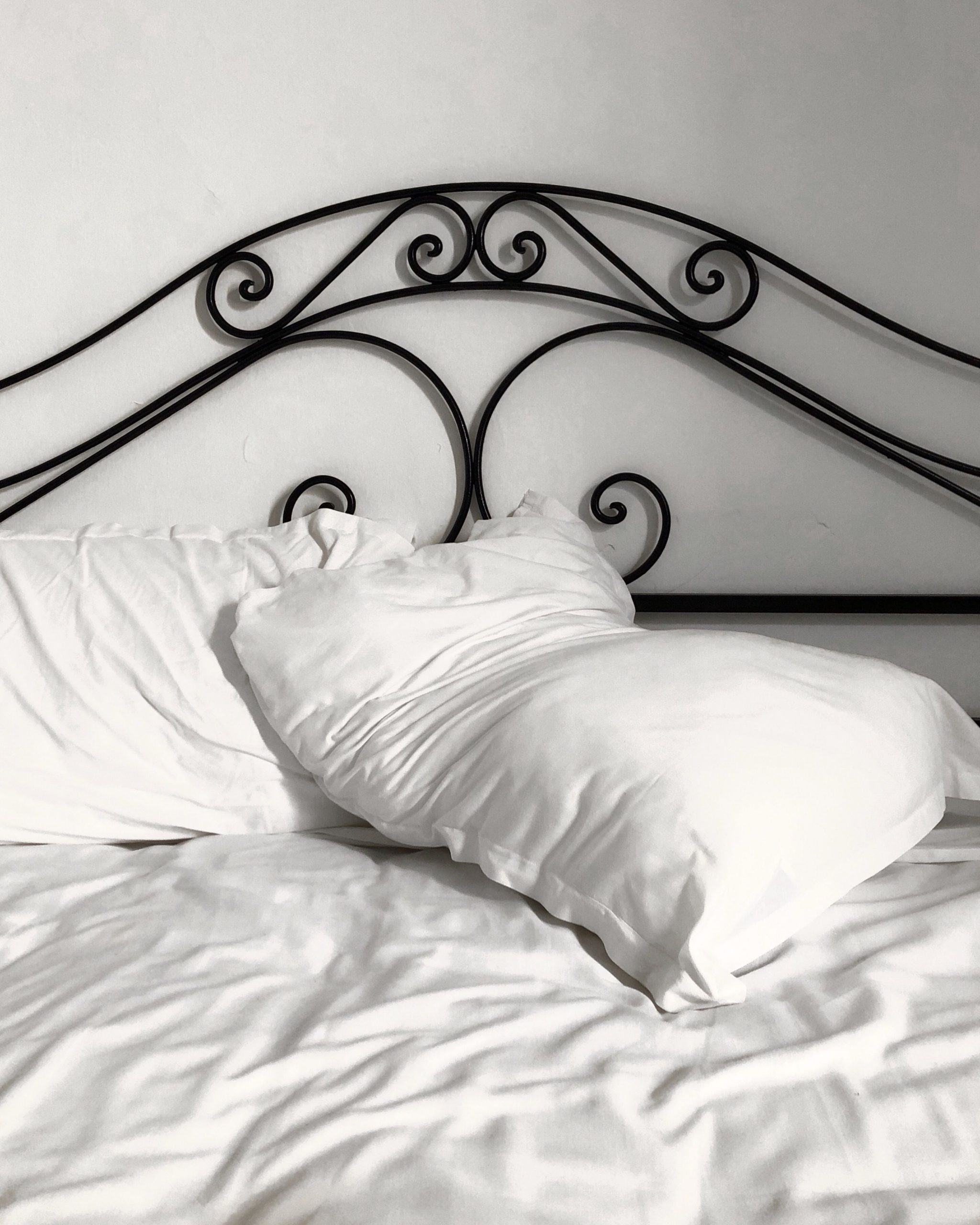A close-up of a black iron headboard with white pillows and sheets, offering a cozy and inviting atmosphere.