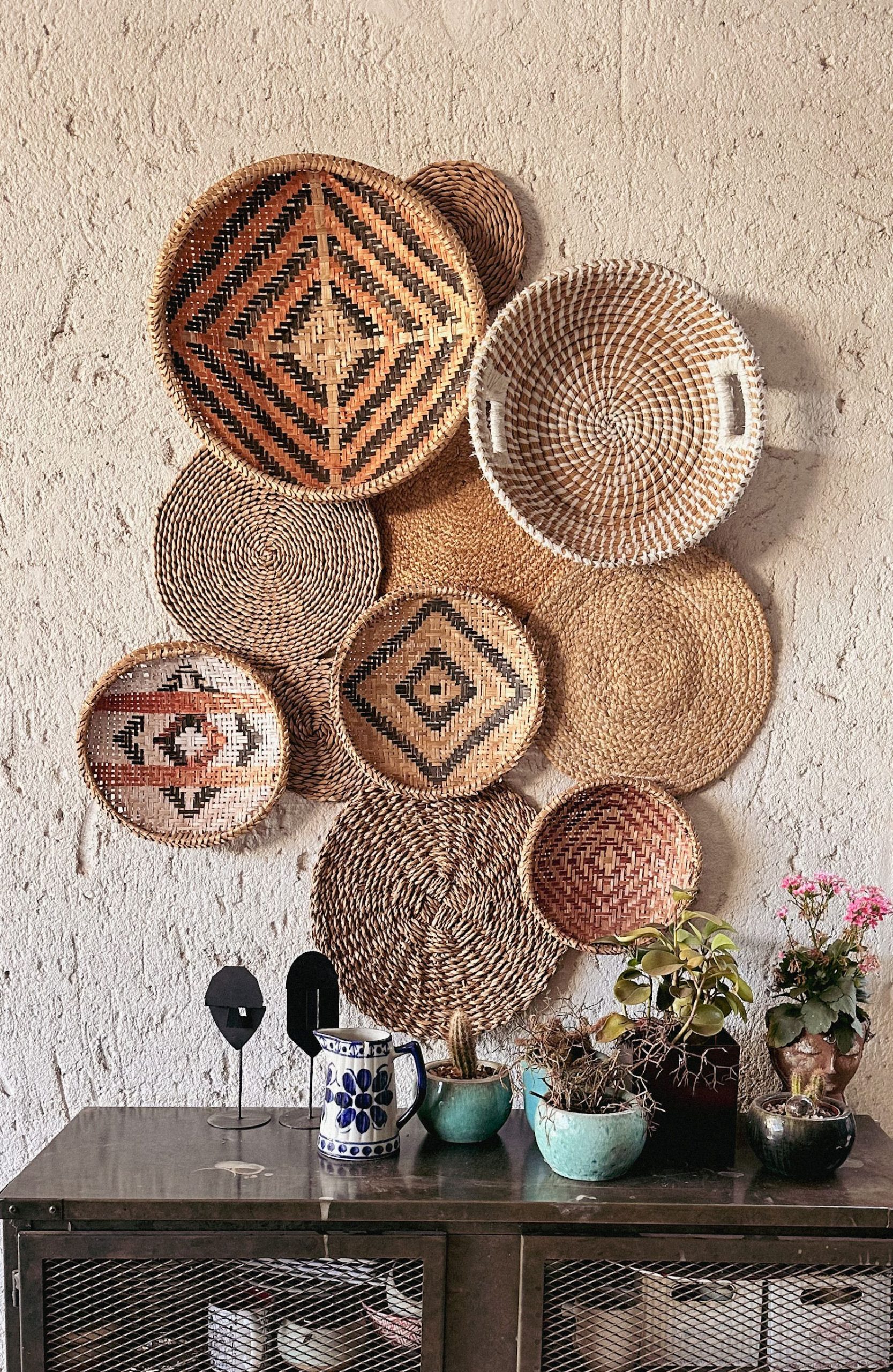 A collection of wicker baskets hang on the wall with flowerpots and plants below, showcasing rustic decor.