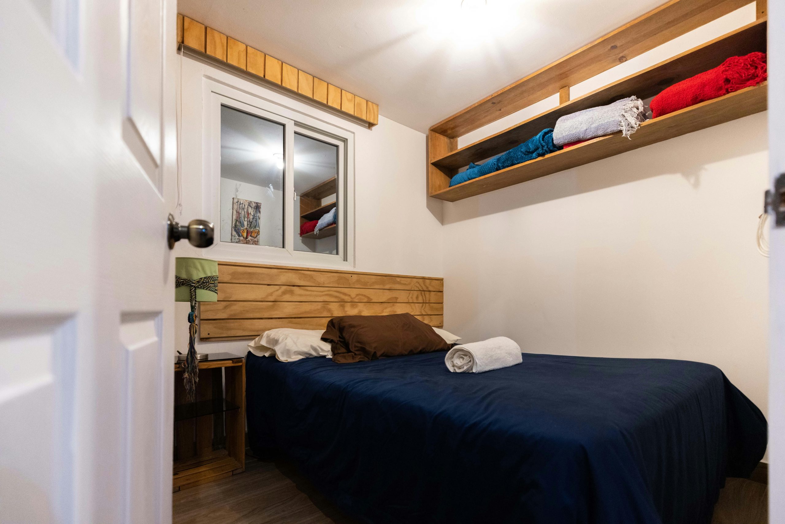 A cozy bedroom featuring a comfy bed, wooden shelves, and natural light.