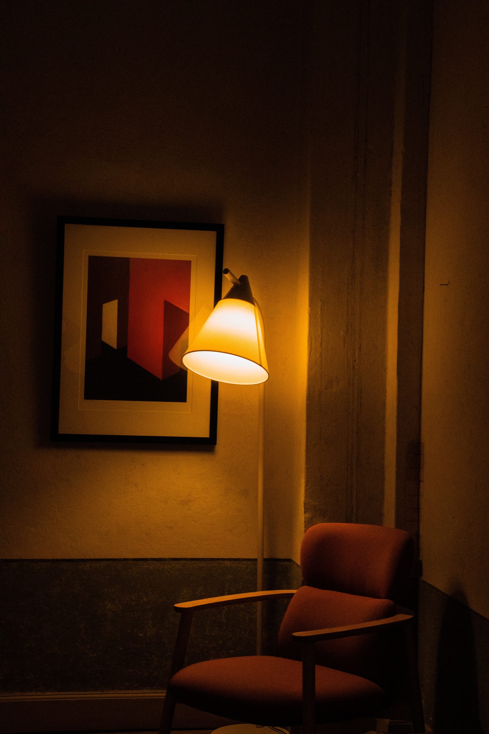 A cozy interior corner with an armchair under warm lamp light beside abstract artwork.