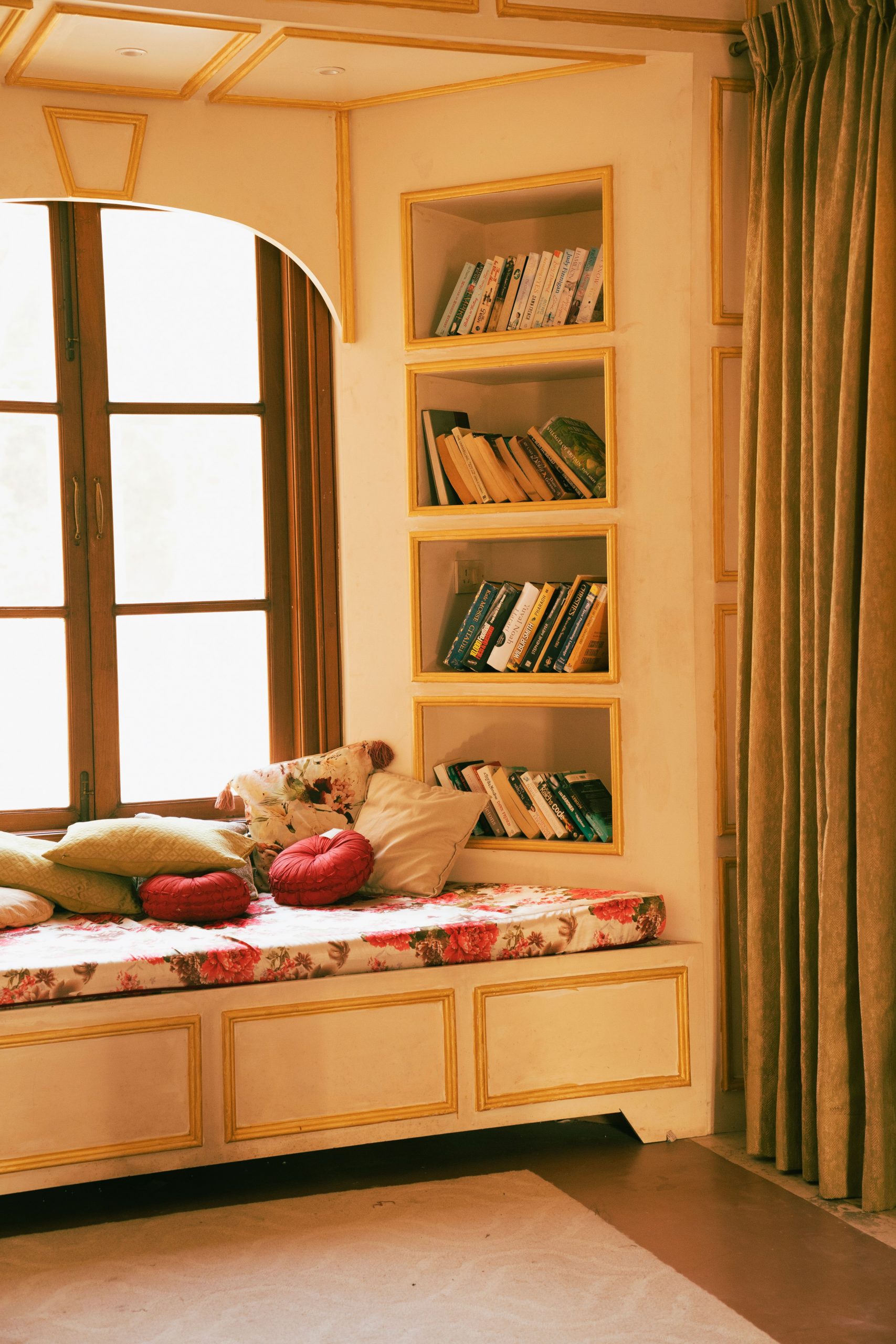 A cozy reading nook with a cushioned window seat, pillows, and built-in bookshelves in a home interior.