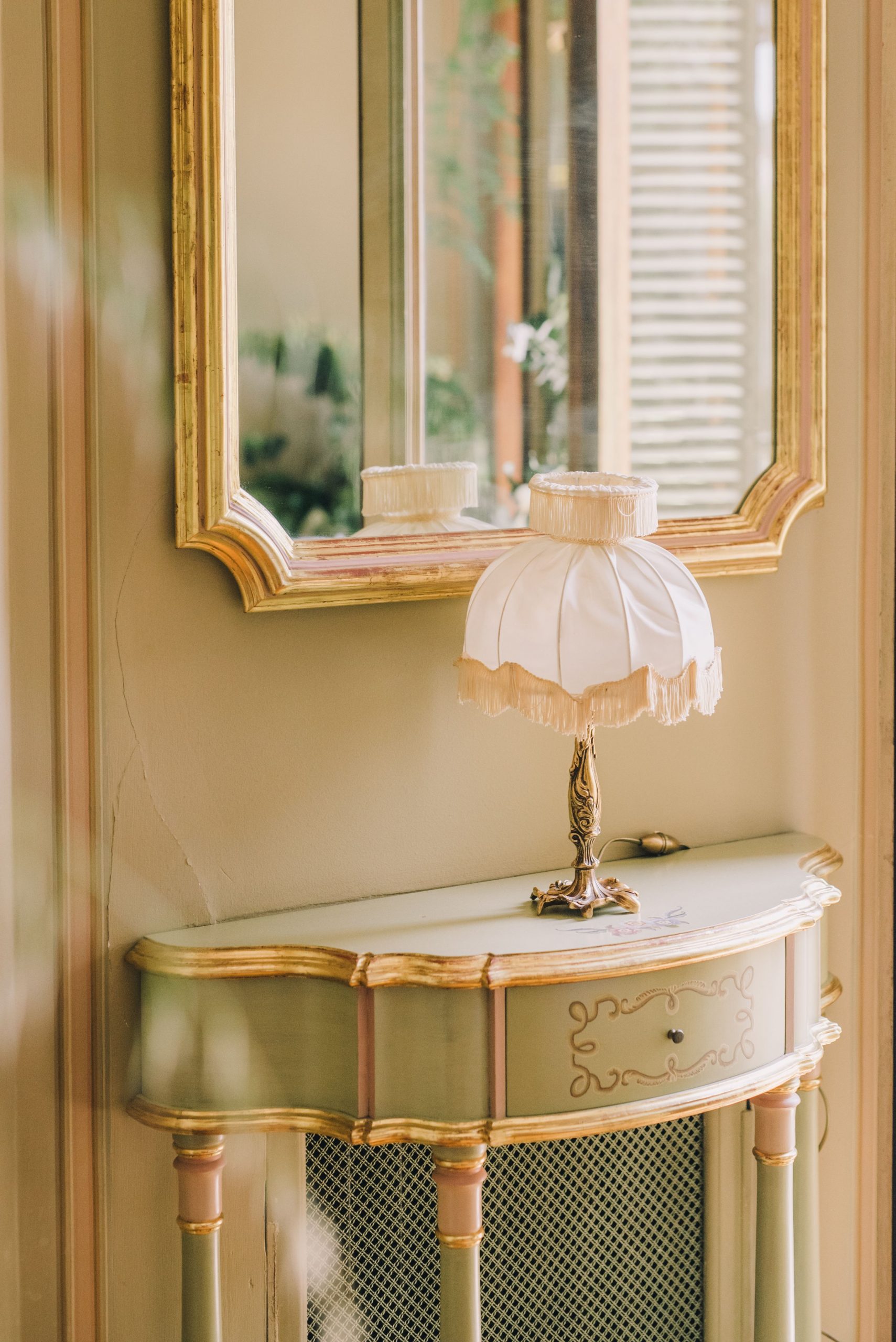 A luxurious vintage room featuring an ornate lamp and a stylish mirror reflecting the elegant decor.