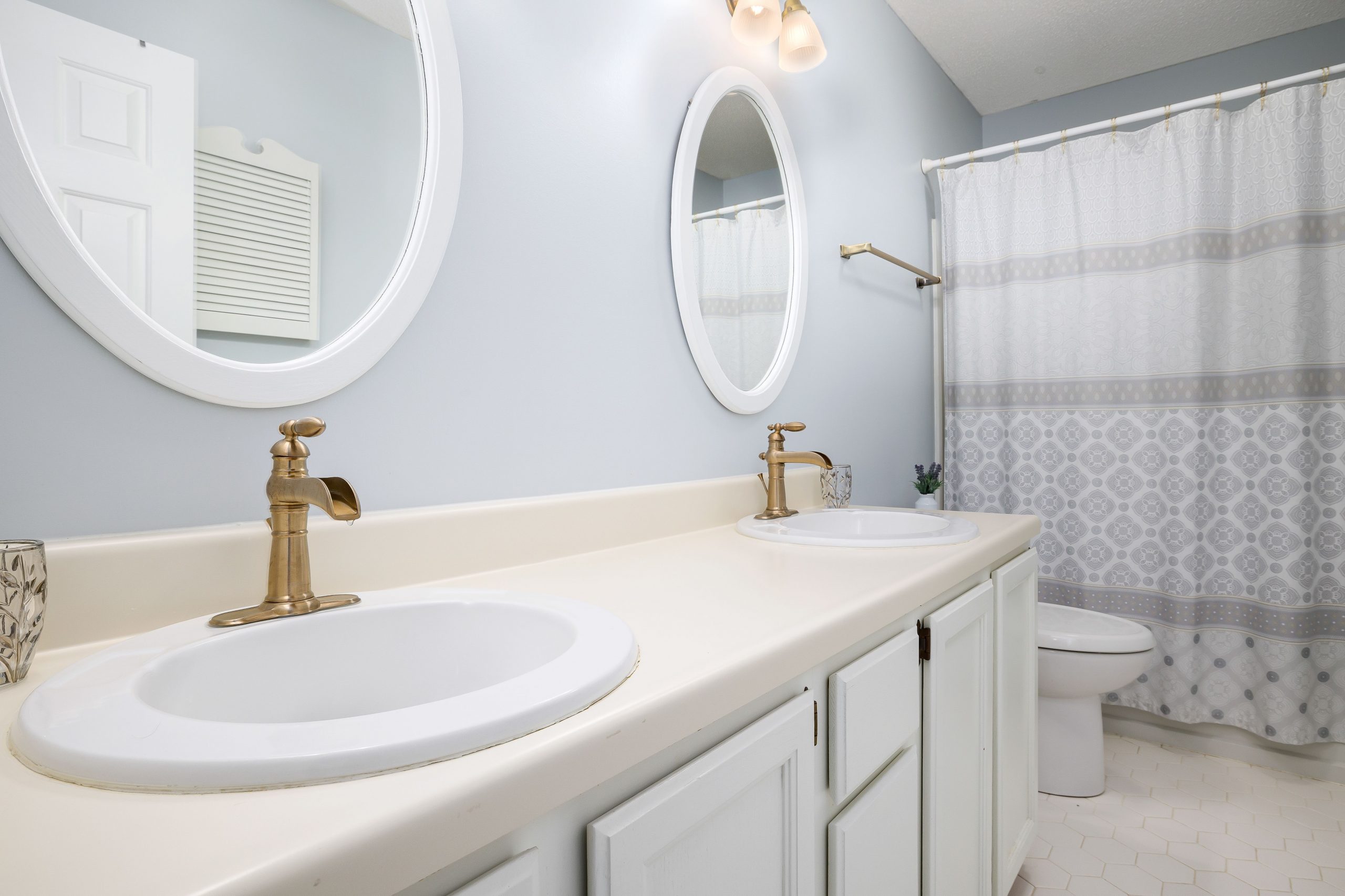 A modern bathroom featuring dual sinks with gold faucets, round mirrors, and a shower curtain.
