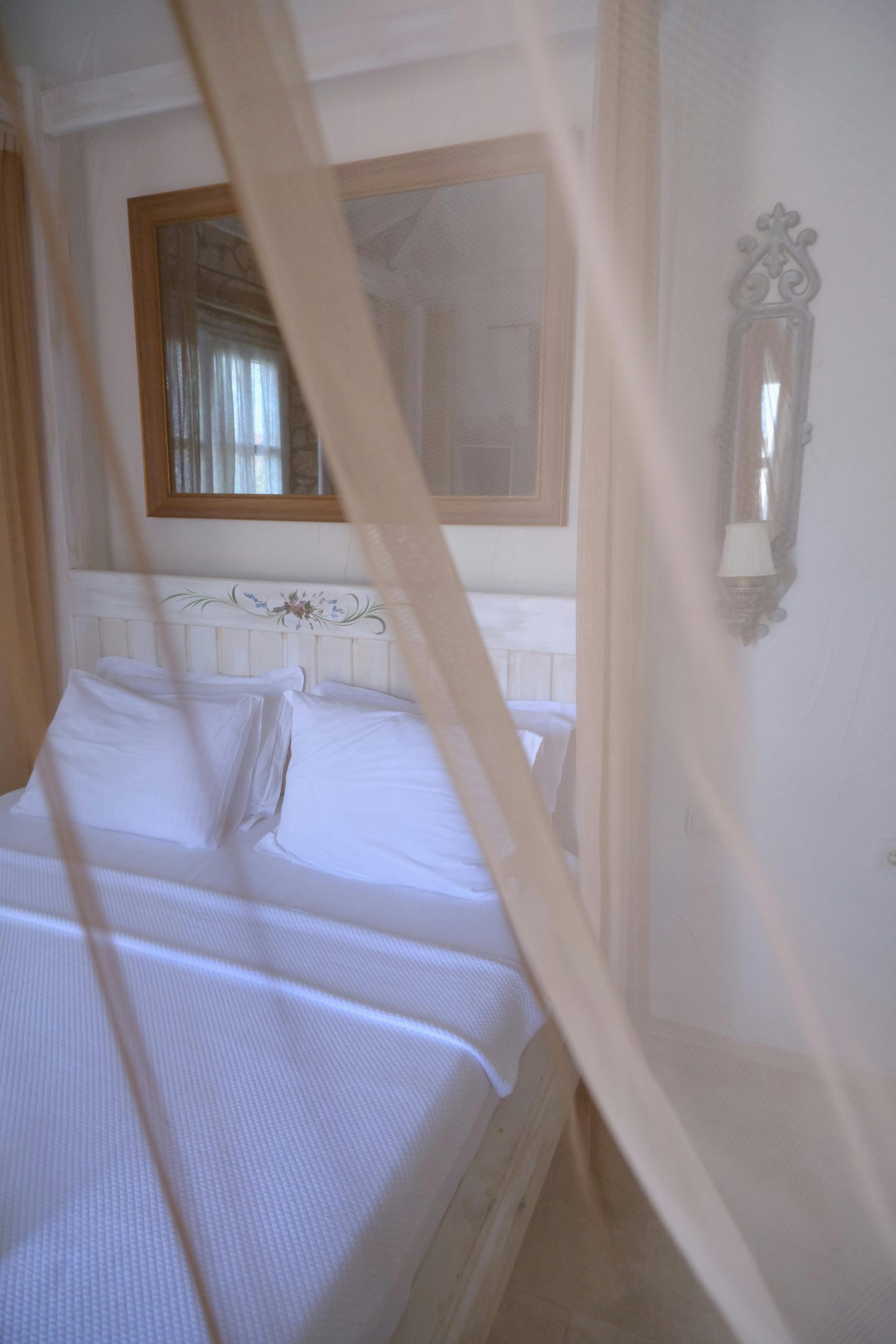 A serene bedroom featuring a bed with soft pillows and a decorative mirror, enhanced by a delicate canopy veil.