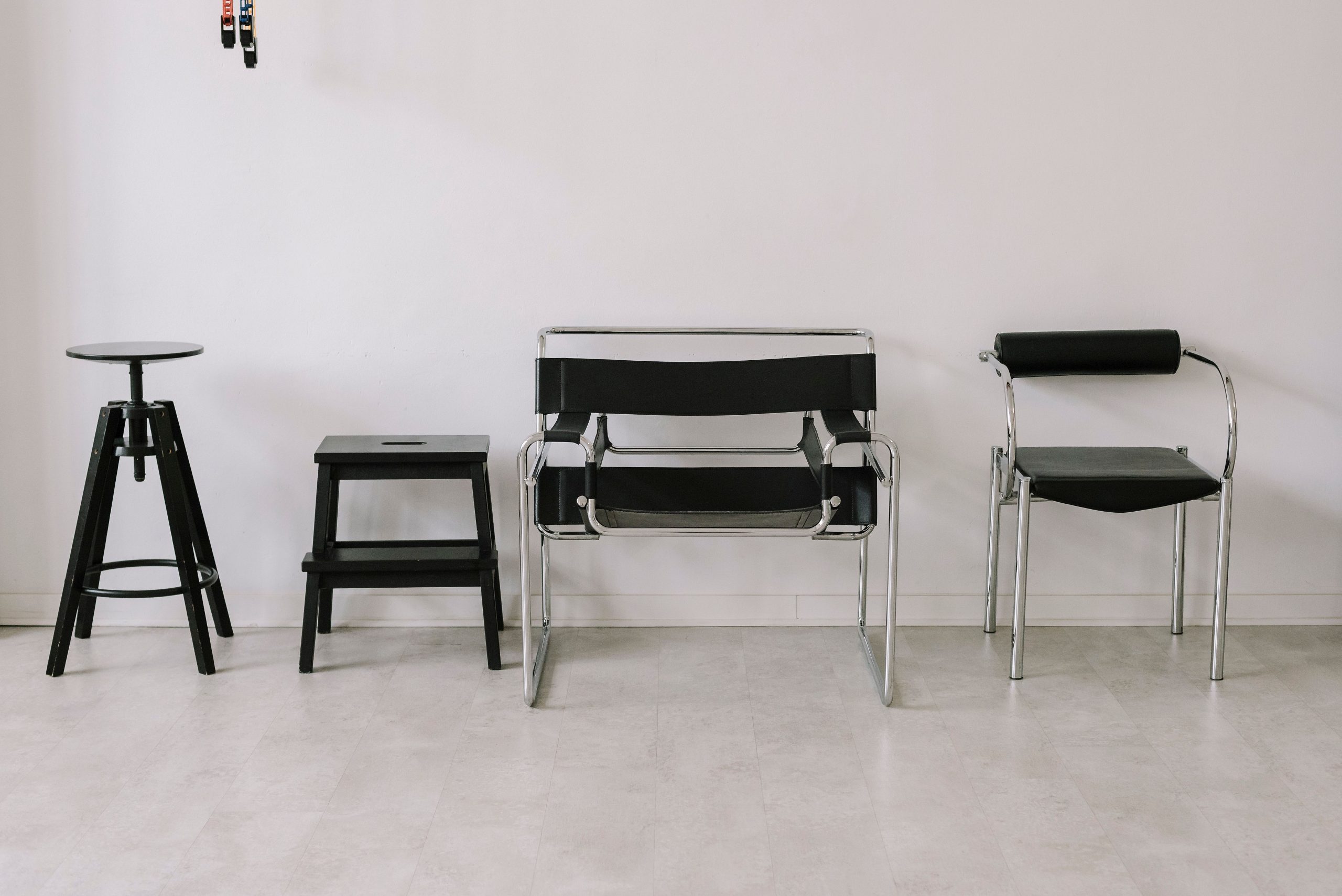 A set of four black chairs in a minimalist indoor setting with a white wall background.