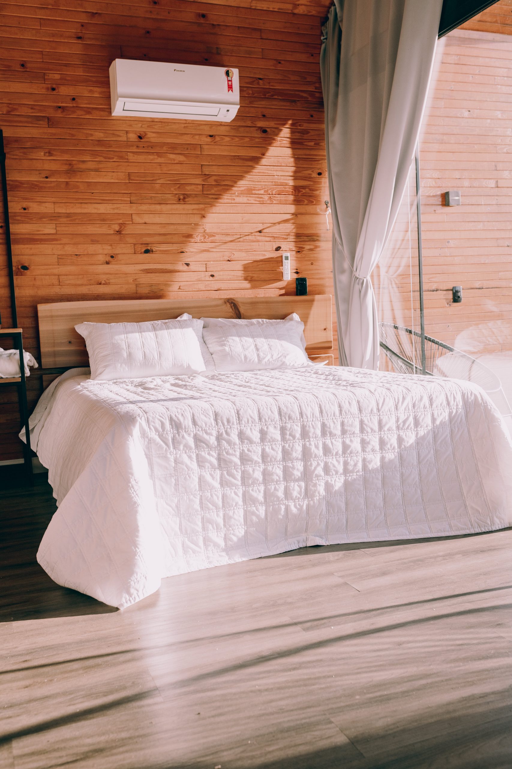 A stylish bedroom featuring a double bed with white bedding, wooden walls, and natural light.