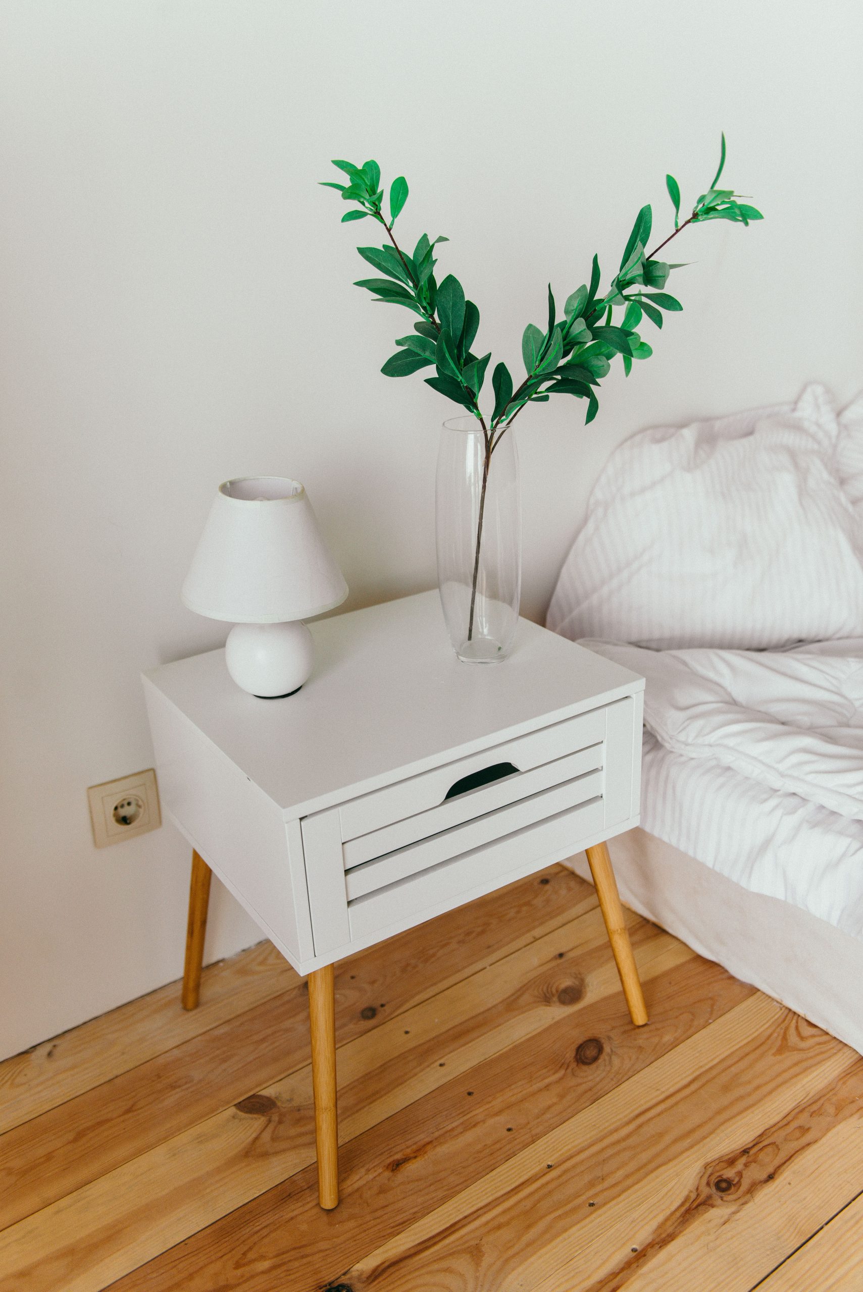 A stylish bedroom showcasing a white nightstand with a vase and lamp, perfect for modern interior design inspiration.