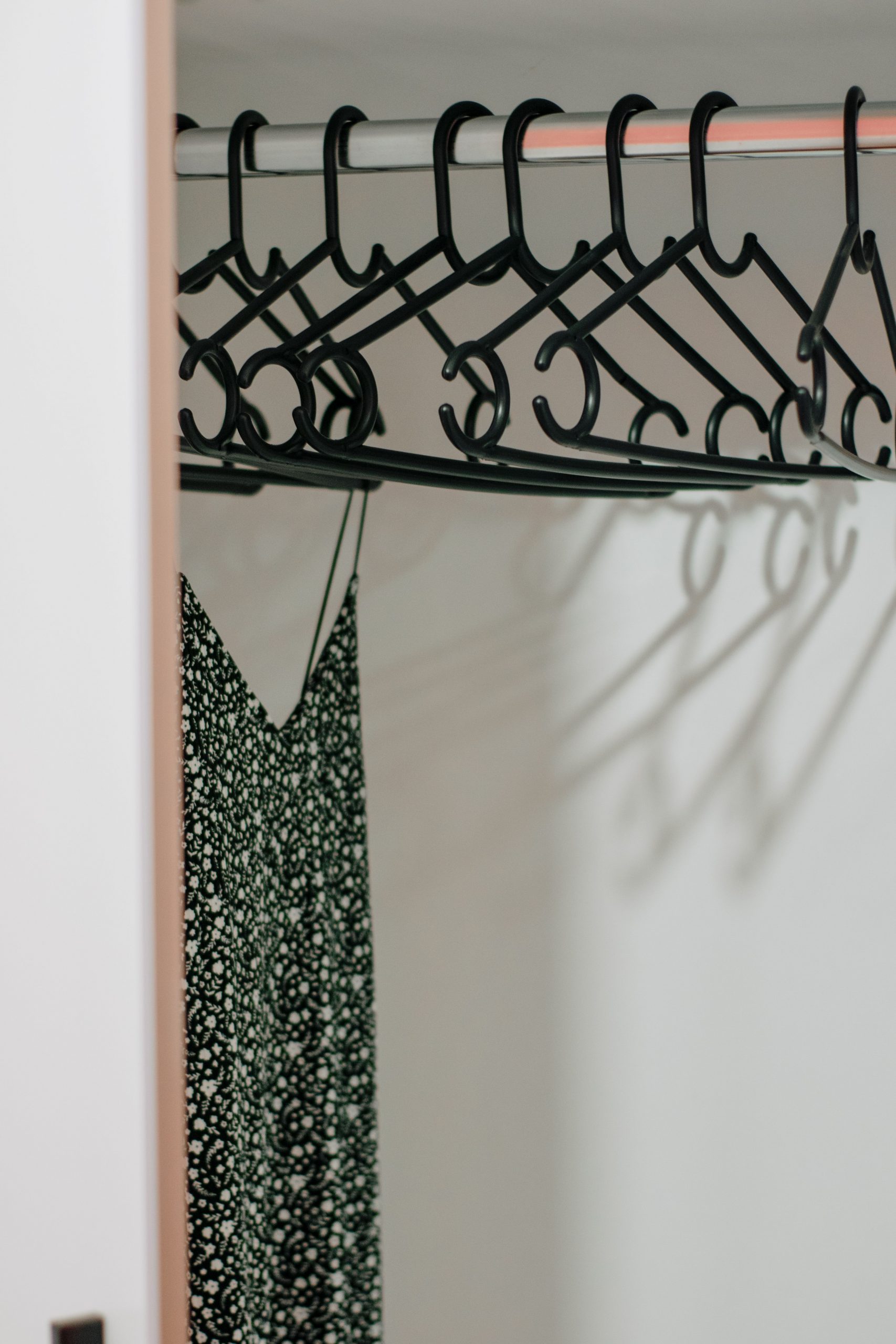 A stylish black dress hangs among black hangers inside a minimalist wardrobe.