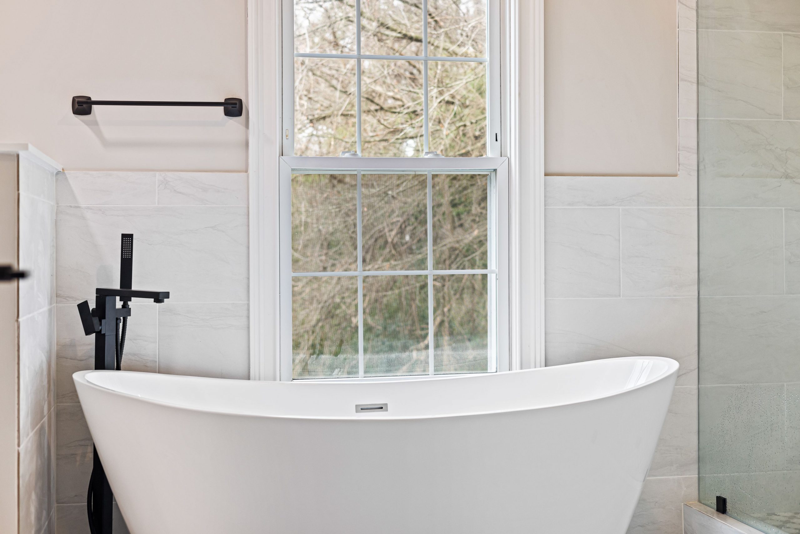 A stylish modern bathroom featuring a freestanding bathtub and large window, ideal for relaxation.