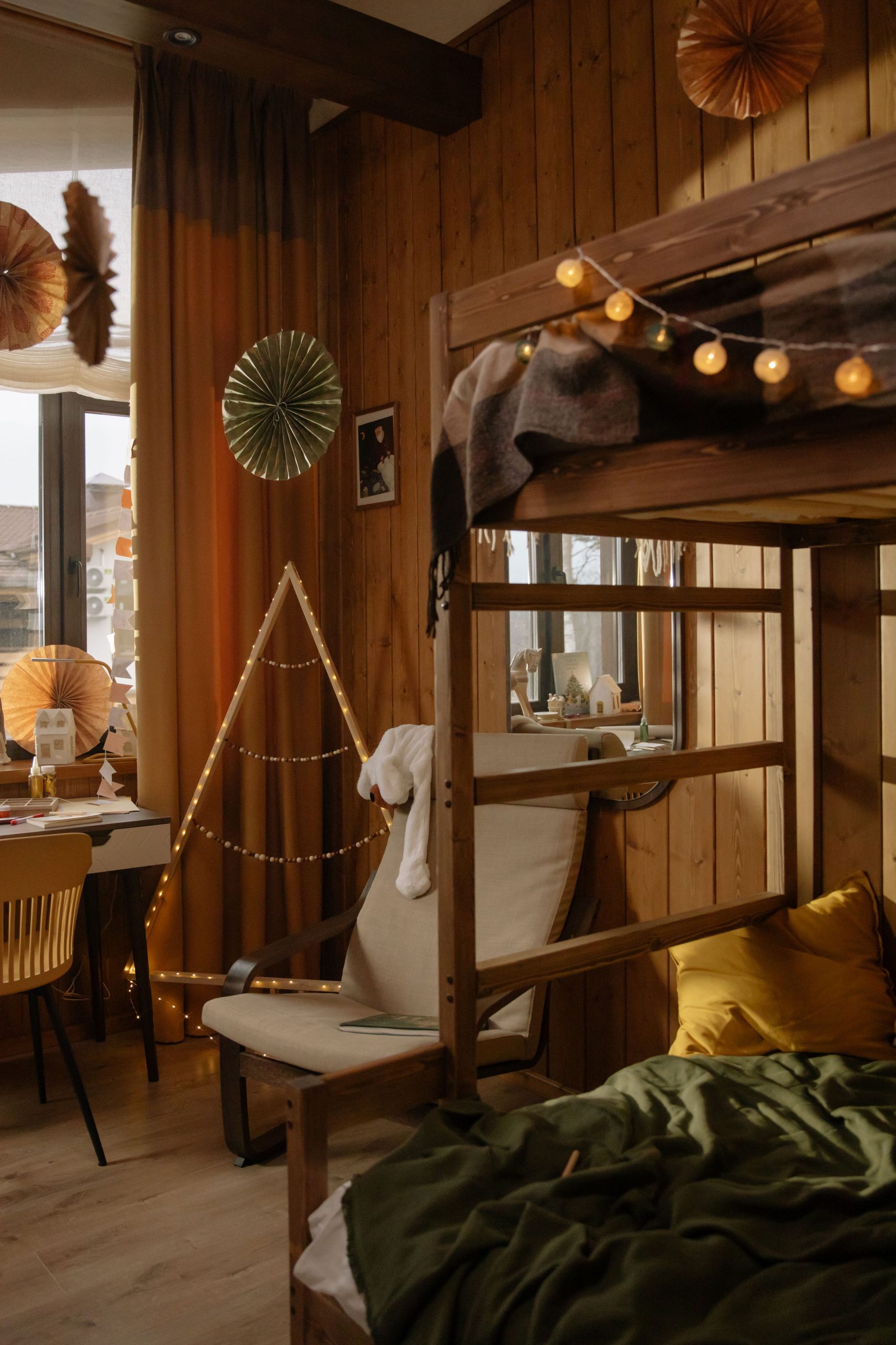 A warm, inviting bedroom with wooden walls, bunk bed, and festive decorations including string lights and paper ornaments.