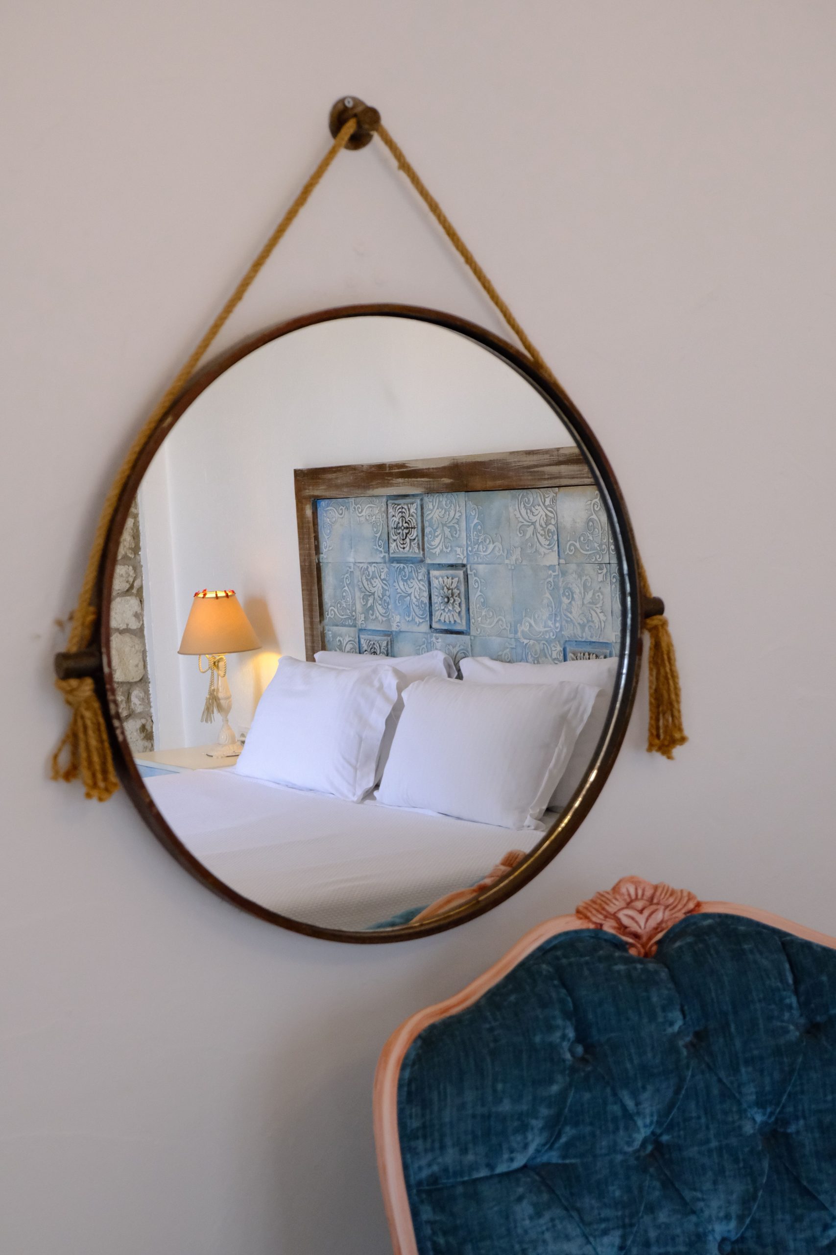 An elegant bedroom mirror reflects cozy bedding and decor, featuring pillows and a stylish armchair.