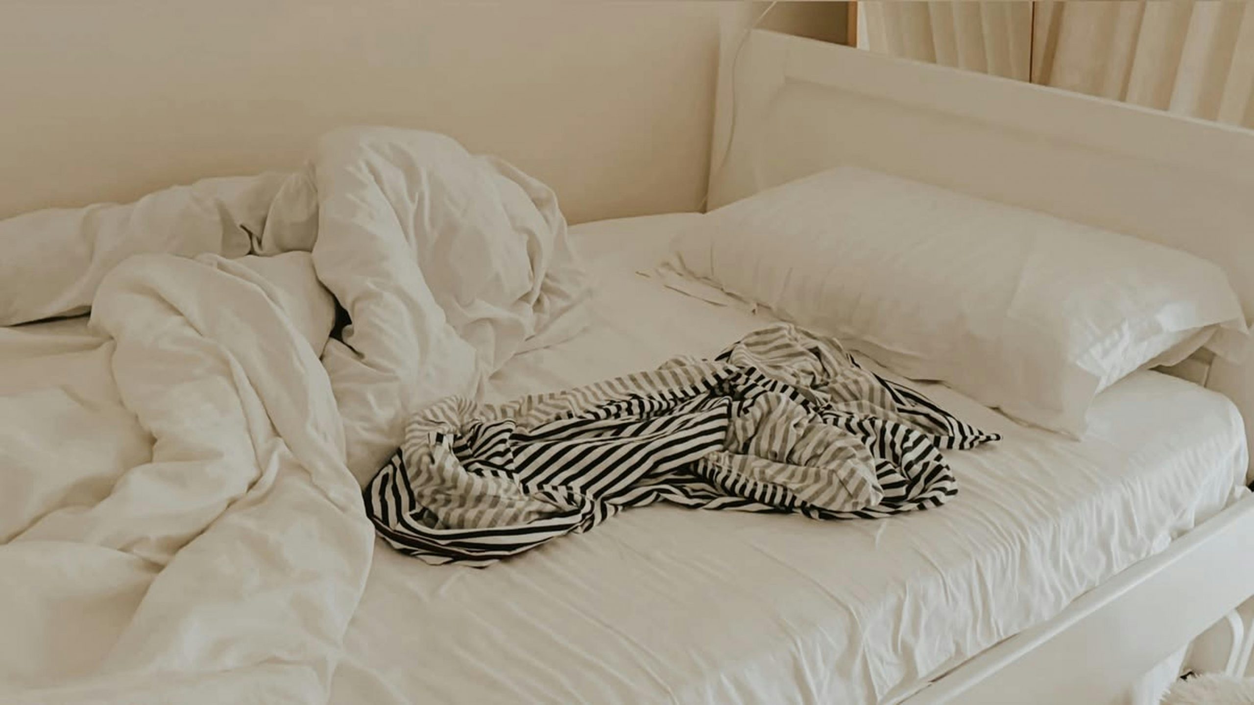 An unmade bed with crumpled linens and a striped shirt adding a cozy feel.