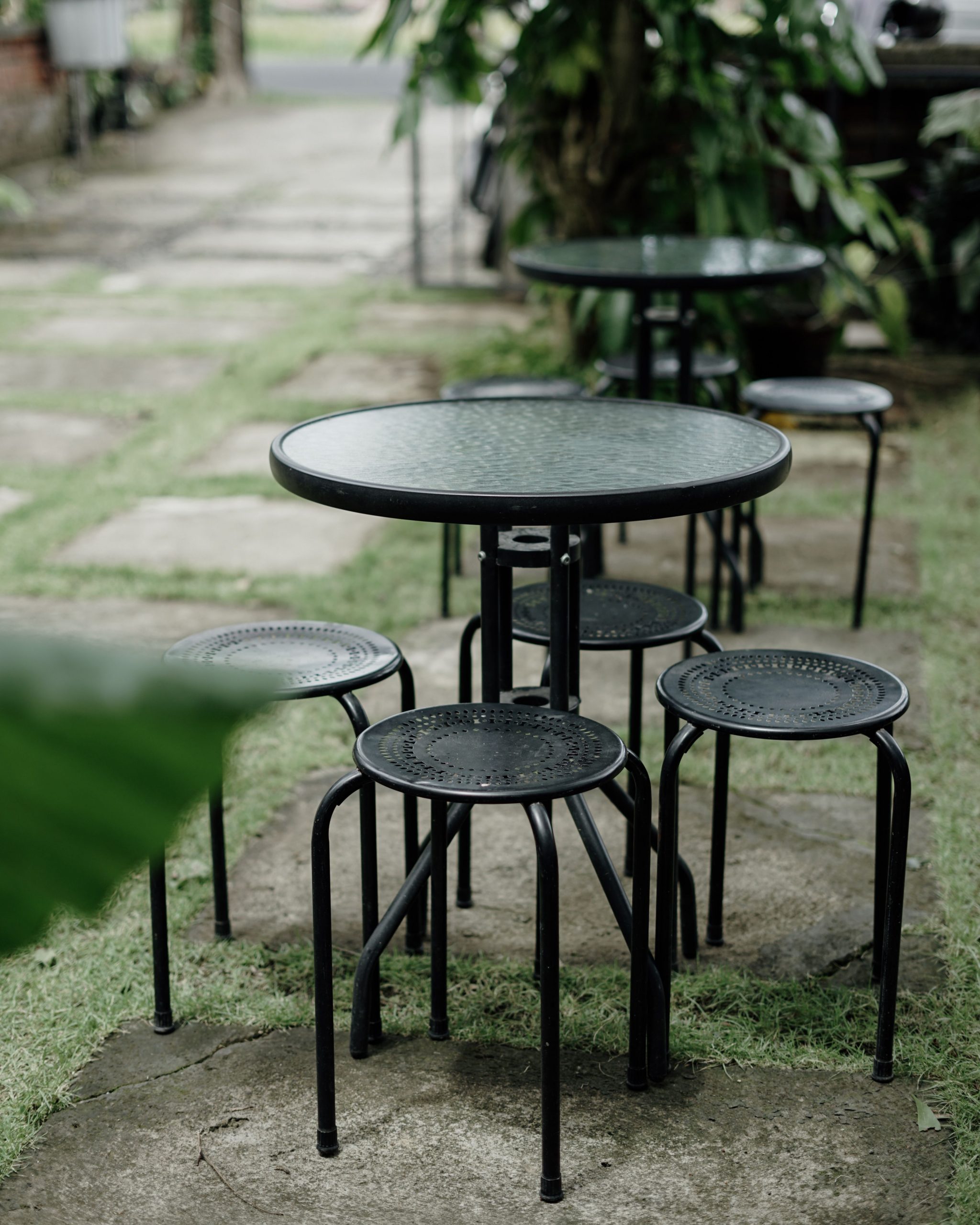 Black metal stools and round glass table set on a lush green outdoor patio.