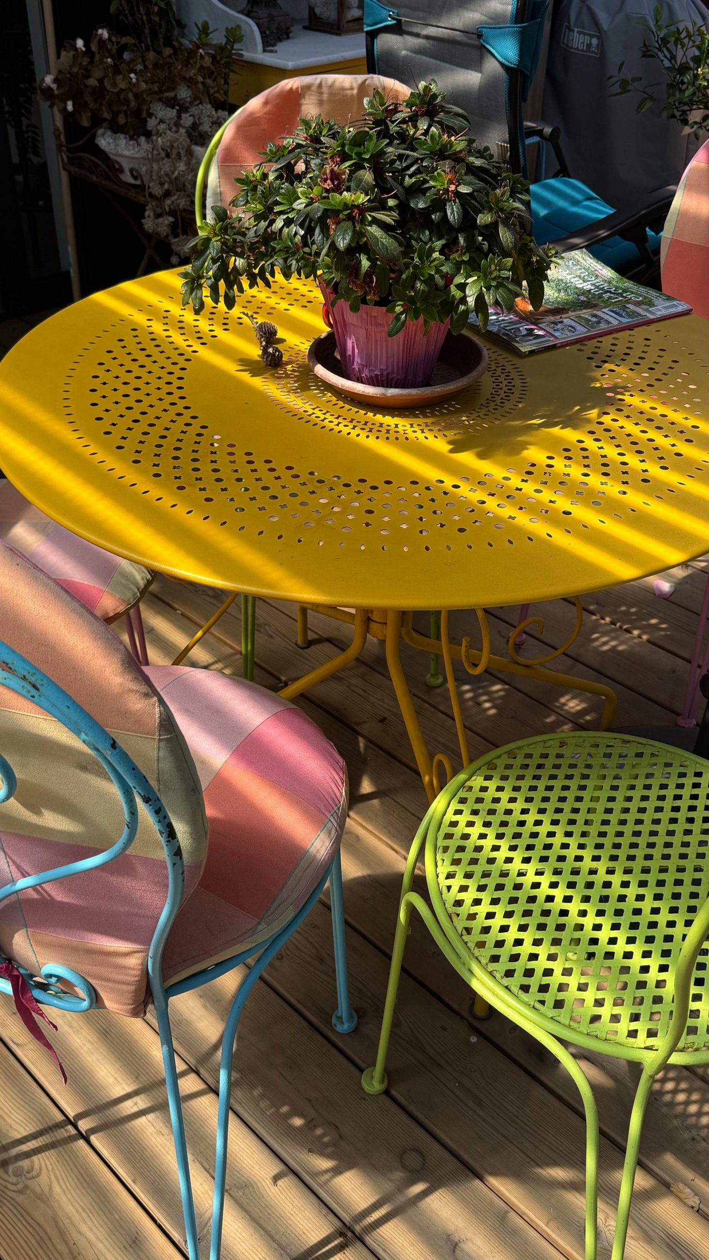 Bright and vibrant outdoor patio setting with a yellow metal table and colorful chairs adorned with a potted plant.