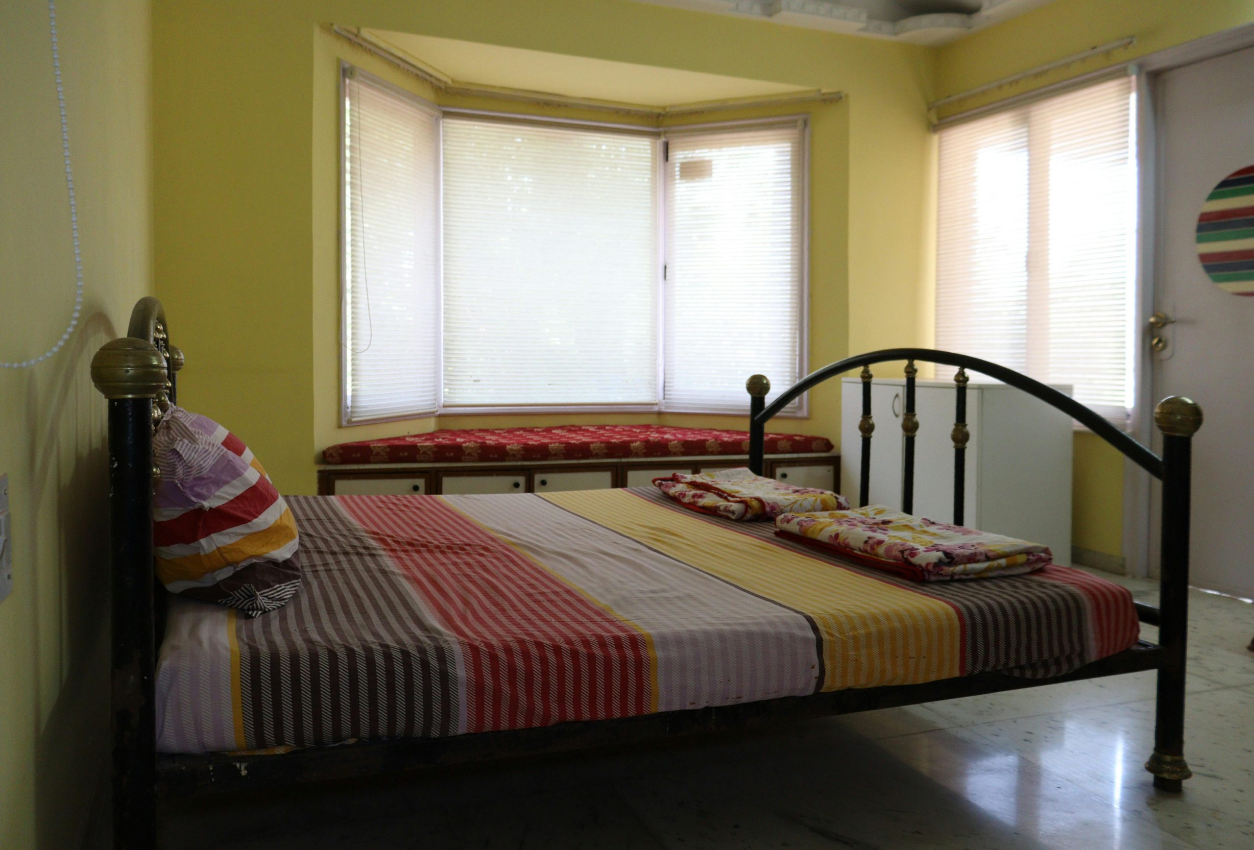 Bright bedroom interior with a striped bedspread, bay windows, and colorful decor, perfect for a cozy ambiance.