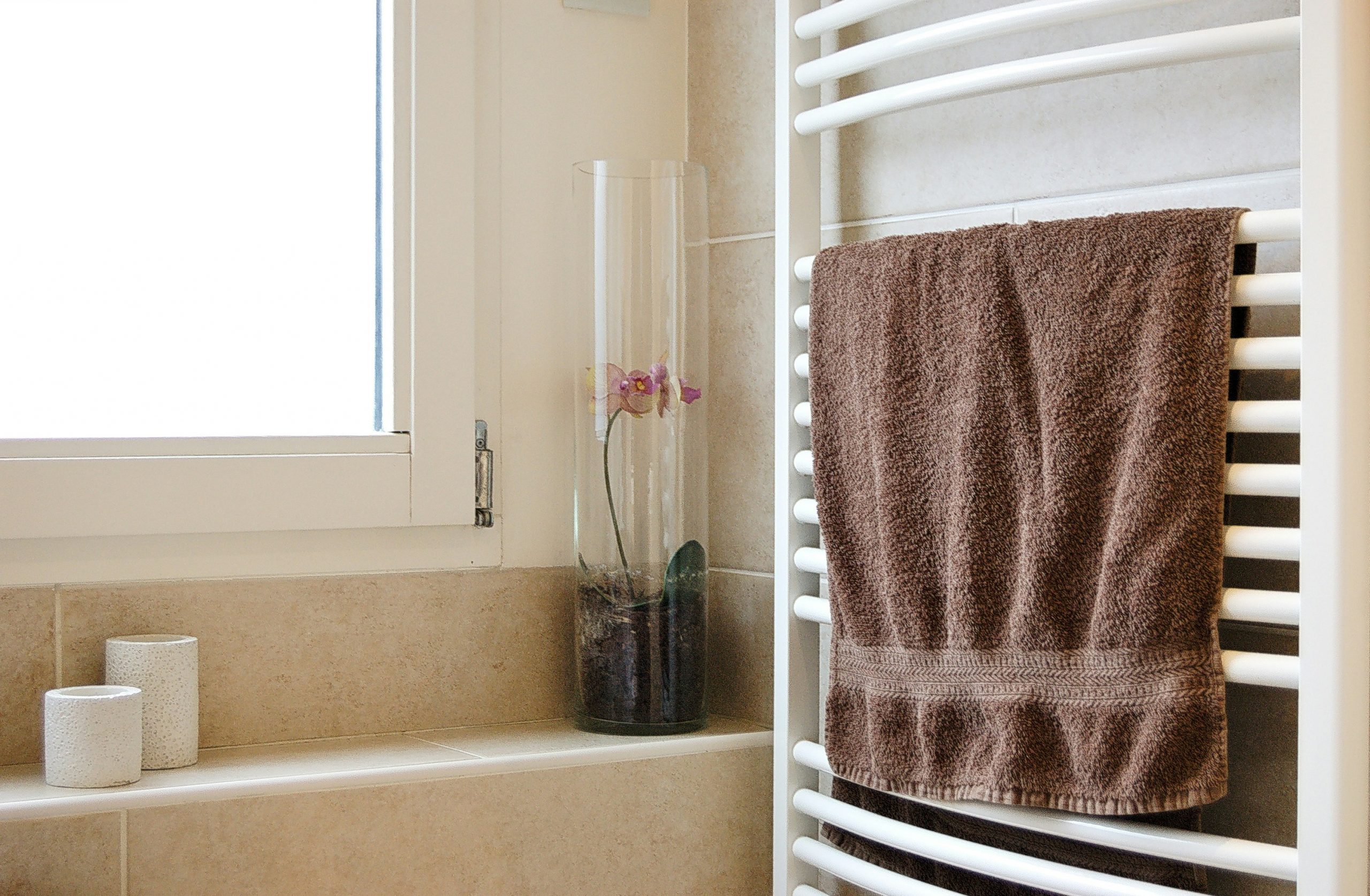 Brown towel hanging on drying rack in classy bathroom with natural stone tiles.