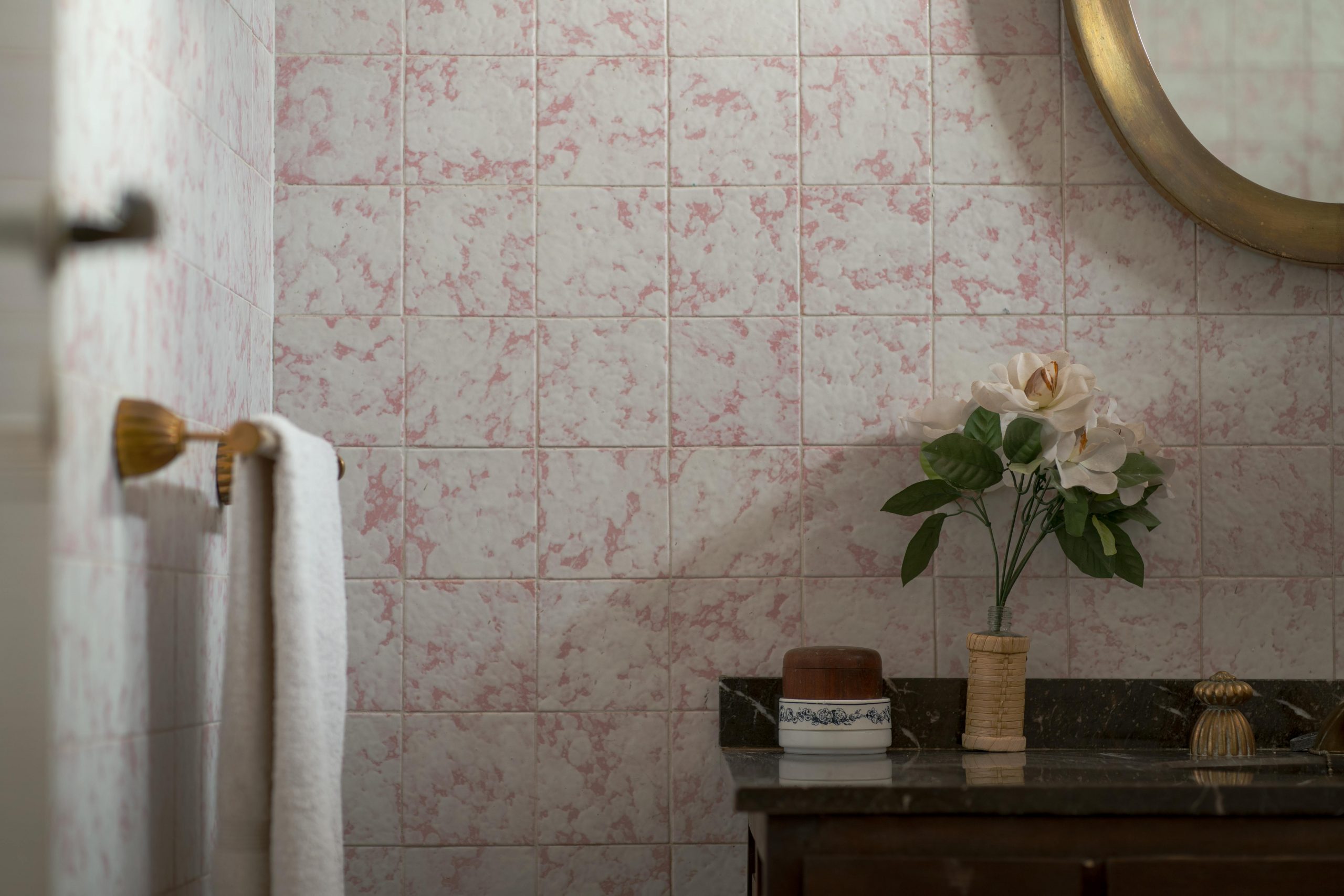 Charming bathroom scene with vintage tiles, a round mirror, and floral decoration.