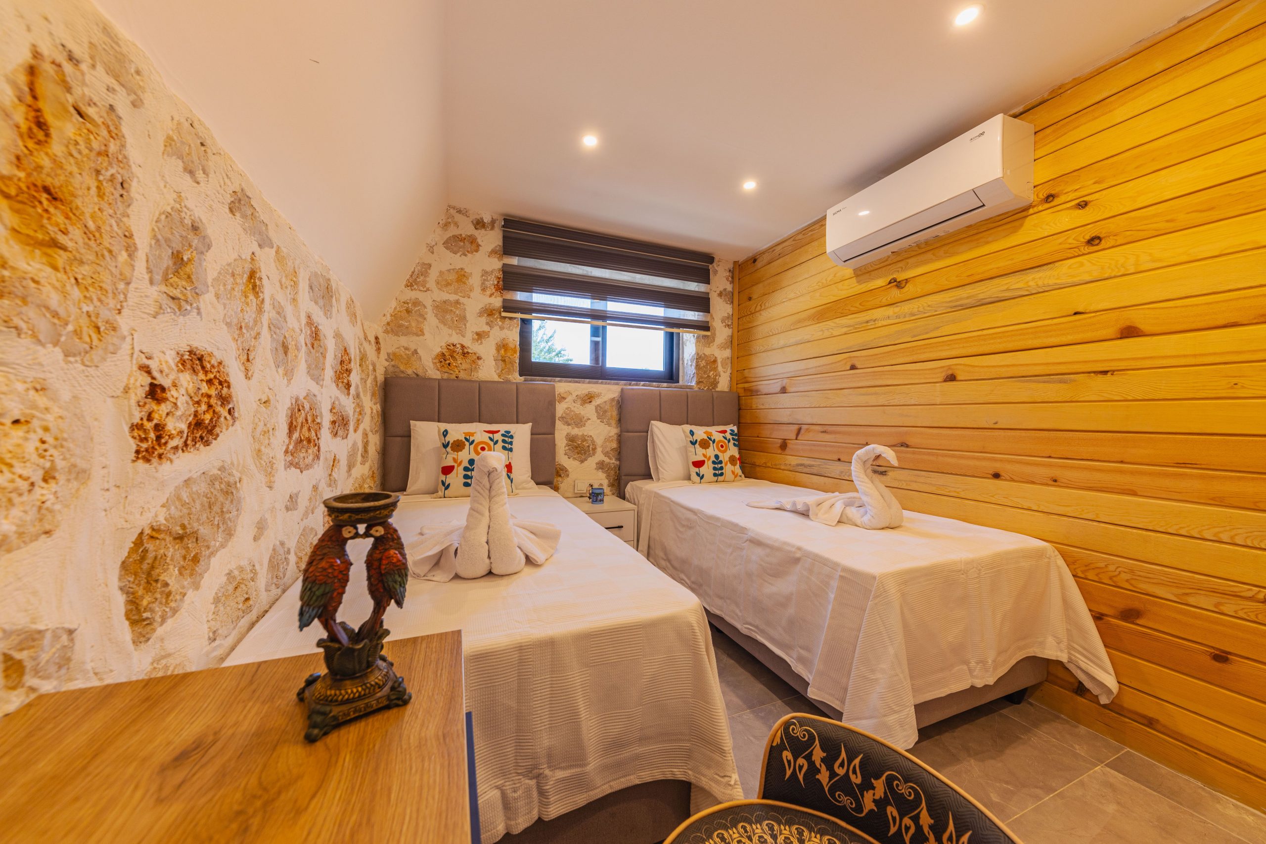 Charming hotel room featuring cozy twin beds, decorative swan towels, and rustic wooden walls.