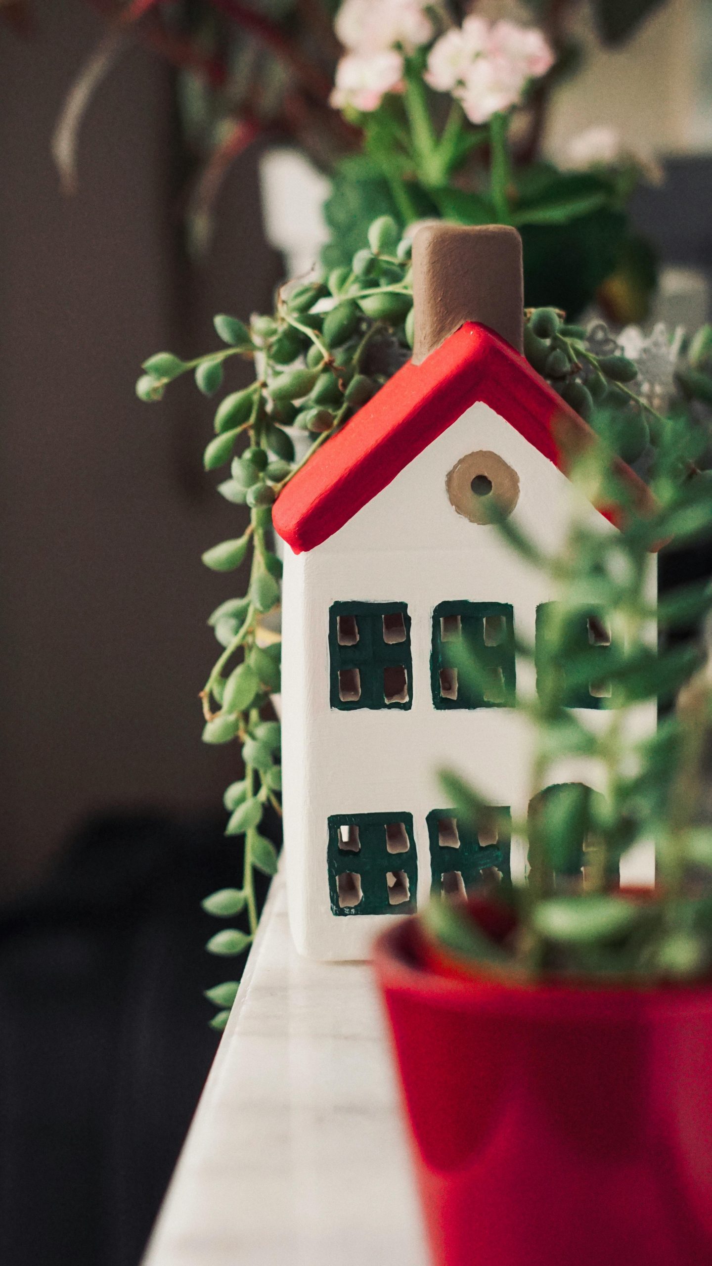 Close-up of a decorative miniature house surrounded by lush green potted plants on a ledge.